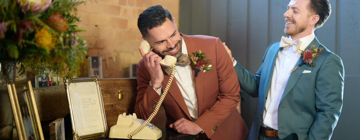 man speaking into audio guestbook at wedding with groomsman supporting him