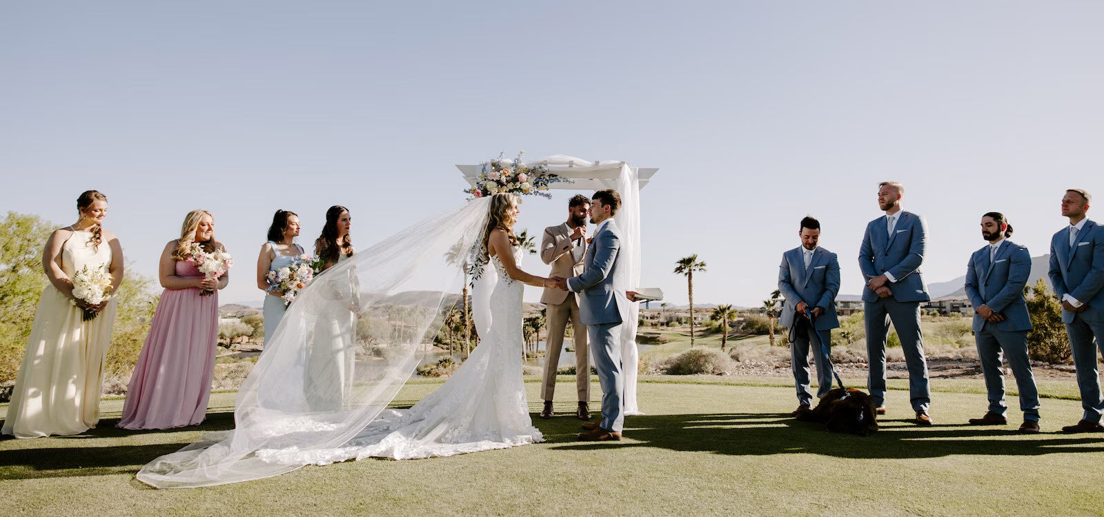 A bride and groom create a lasting wedding memory as they exchange vows during a sunny outdoor ceremony with their wedding party.