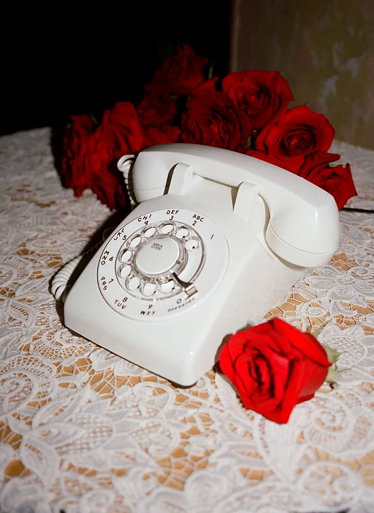 White audio guestbook phone sits with red roses on a guest book table