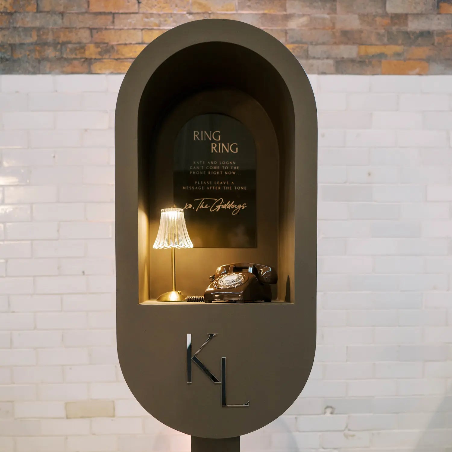 Decorative phone booth with a brown vintage telephone and lamp against a brick wall