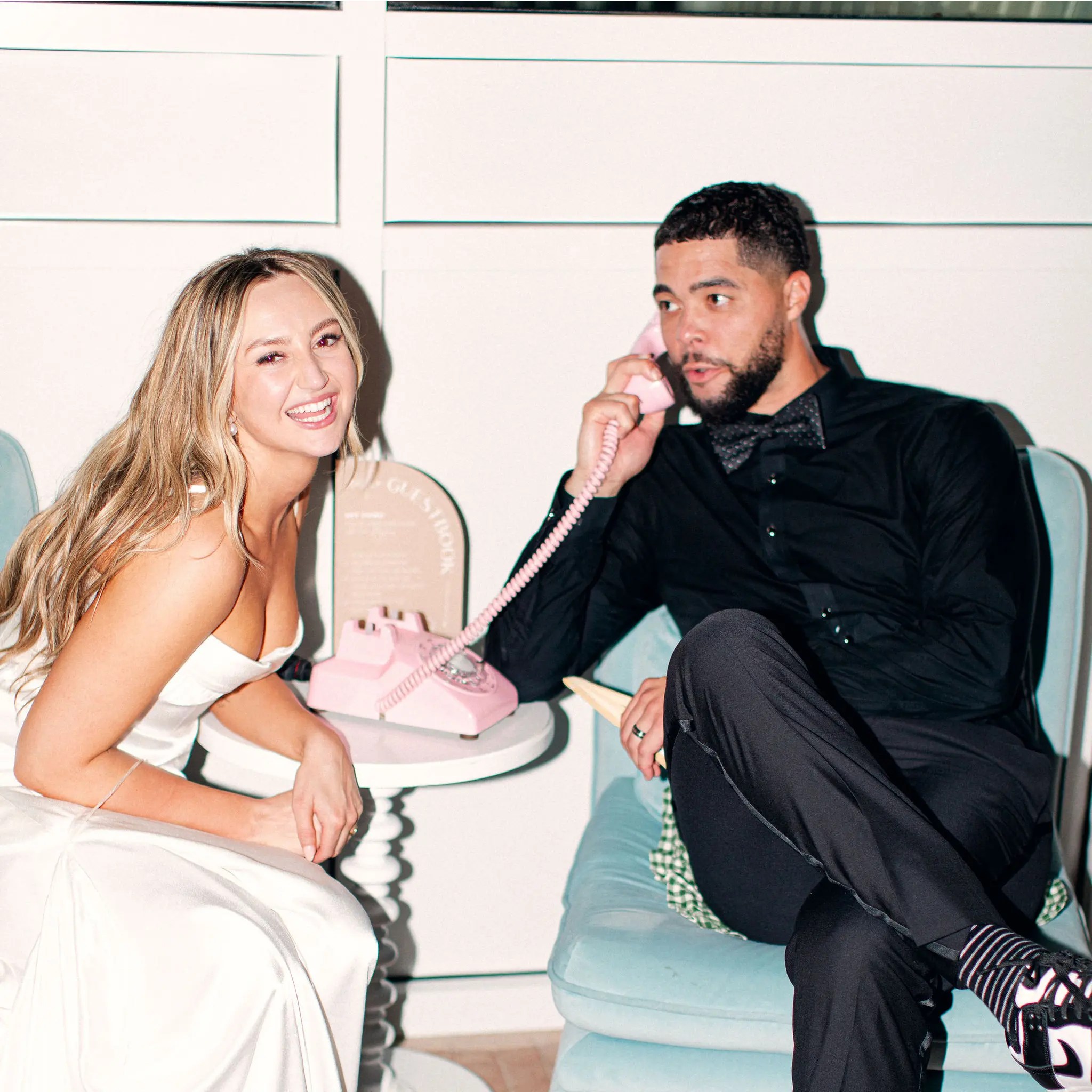 Man in a suit and woman in a white dress sitting together with a pink phone.