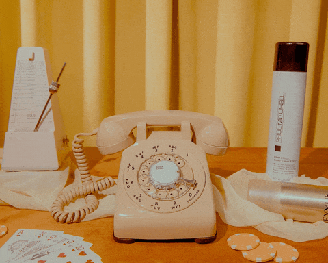 an animated gif video showing a beige rotary phone and various decorations around it on a table and hands interacting with it.