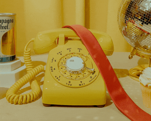 an animated gif video showing a yellow rotary phone audio guestbook and various decorations around it on a table and hands interacting with it.