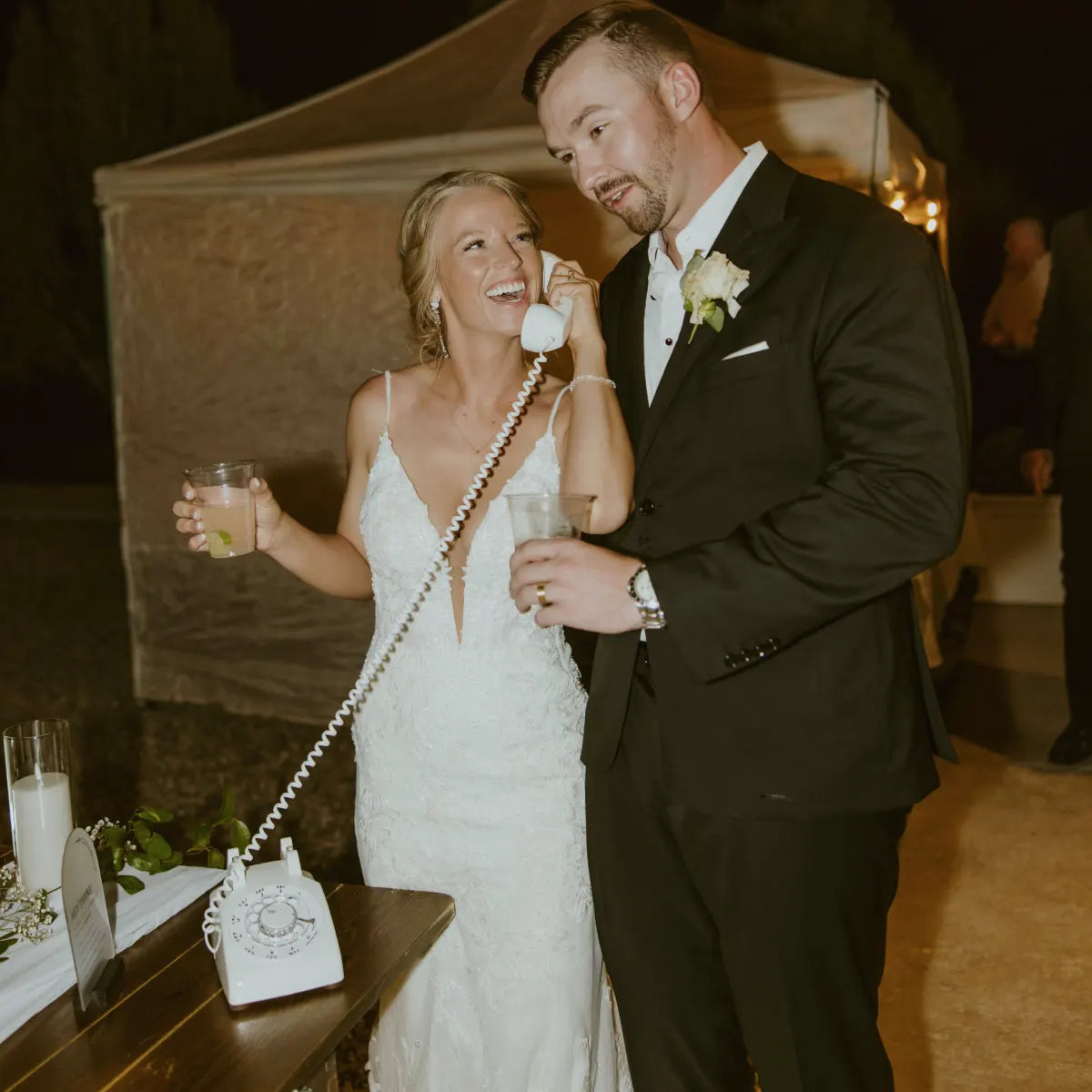Man and woman in wedding attire with a vintage phone at a reception.
