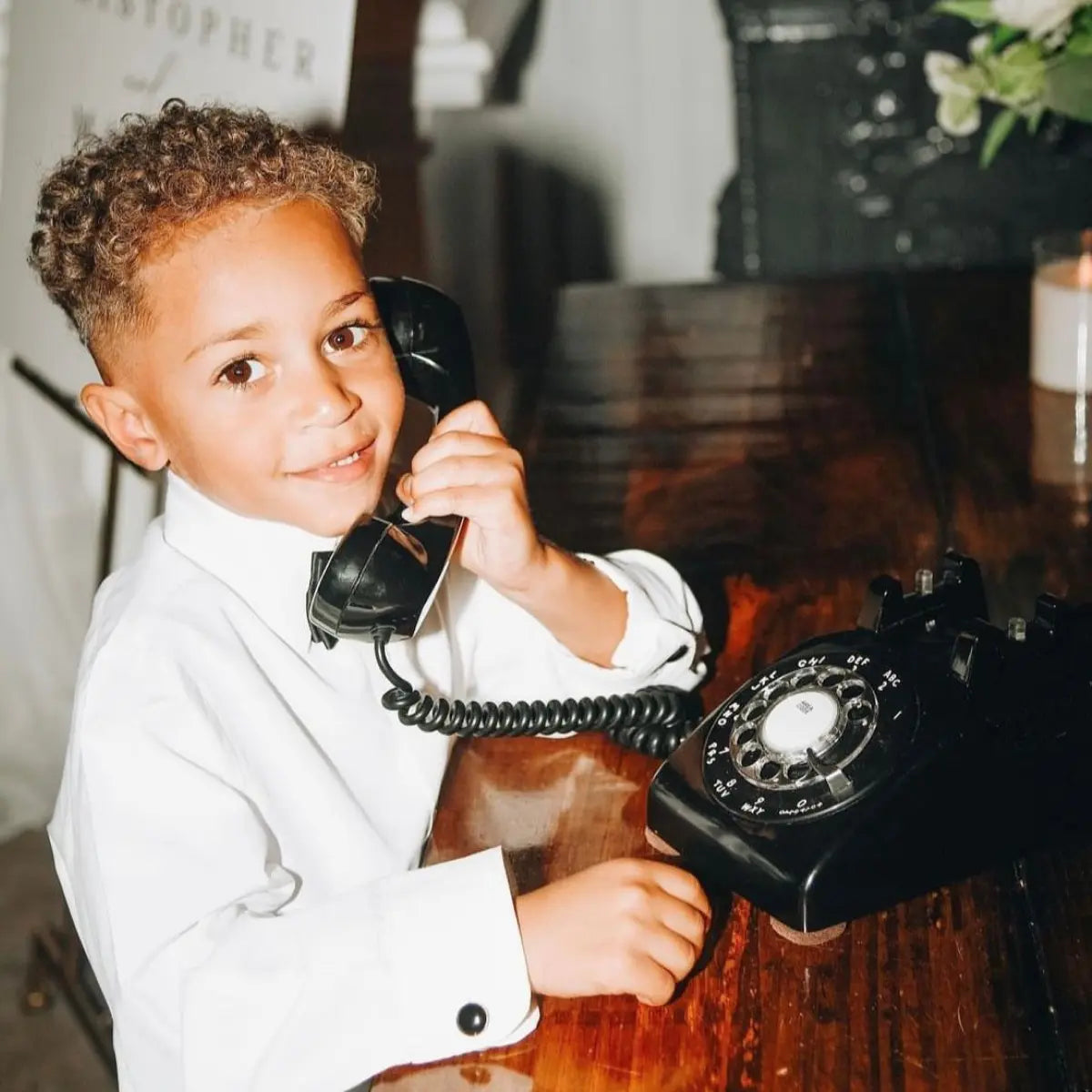 Child in a suit holding an old-fashioned black rotary phone.