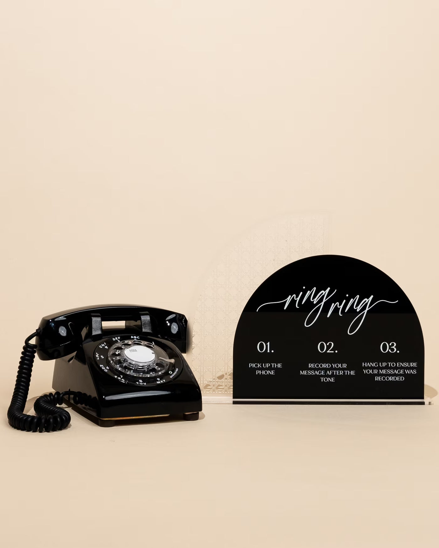 Vintage-style black telephone next to a decorative sign with 'ring ring' text on a beige background