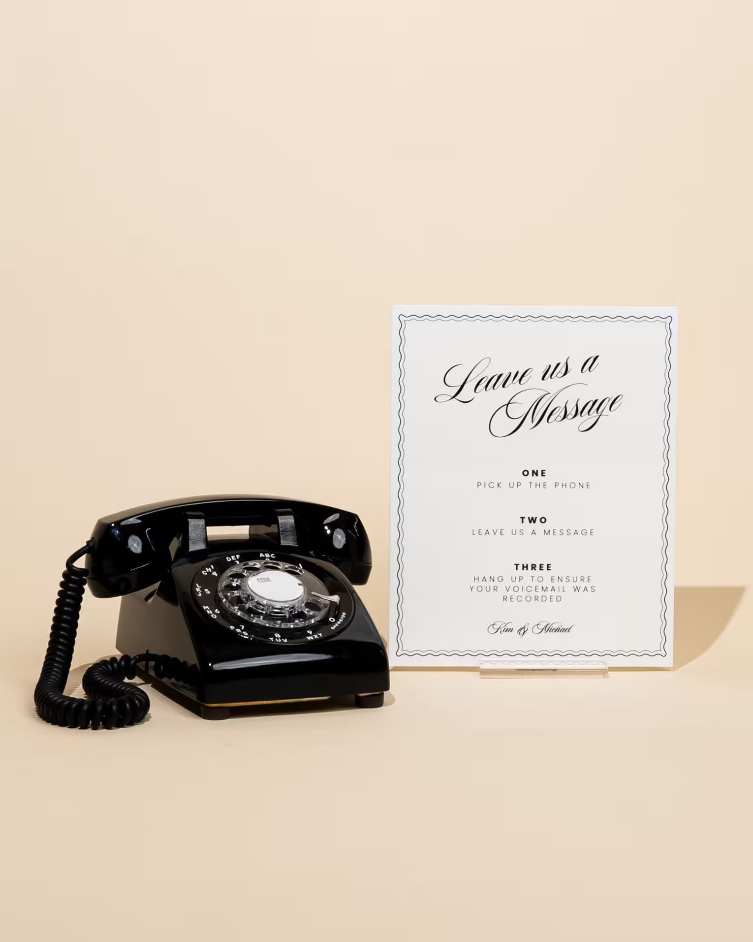 Vintage black rotary phone next to a framed message on a beige background