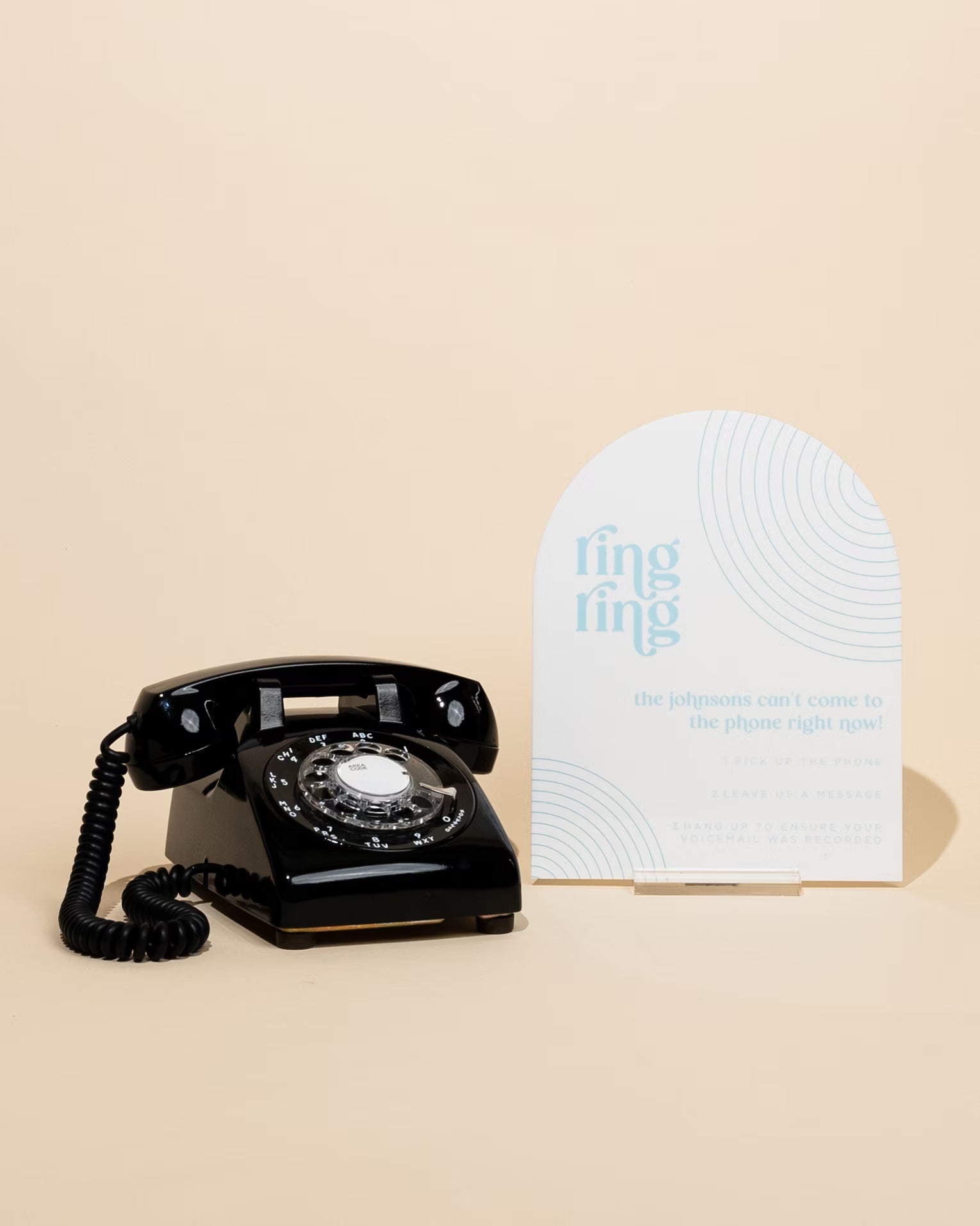 Vintage black rotary phone next to a white card with blue text on a beige background