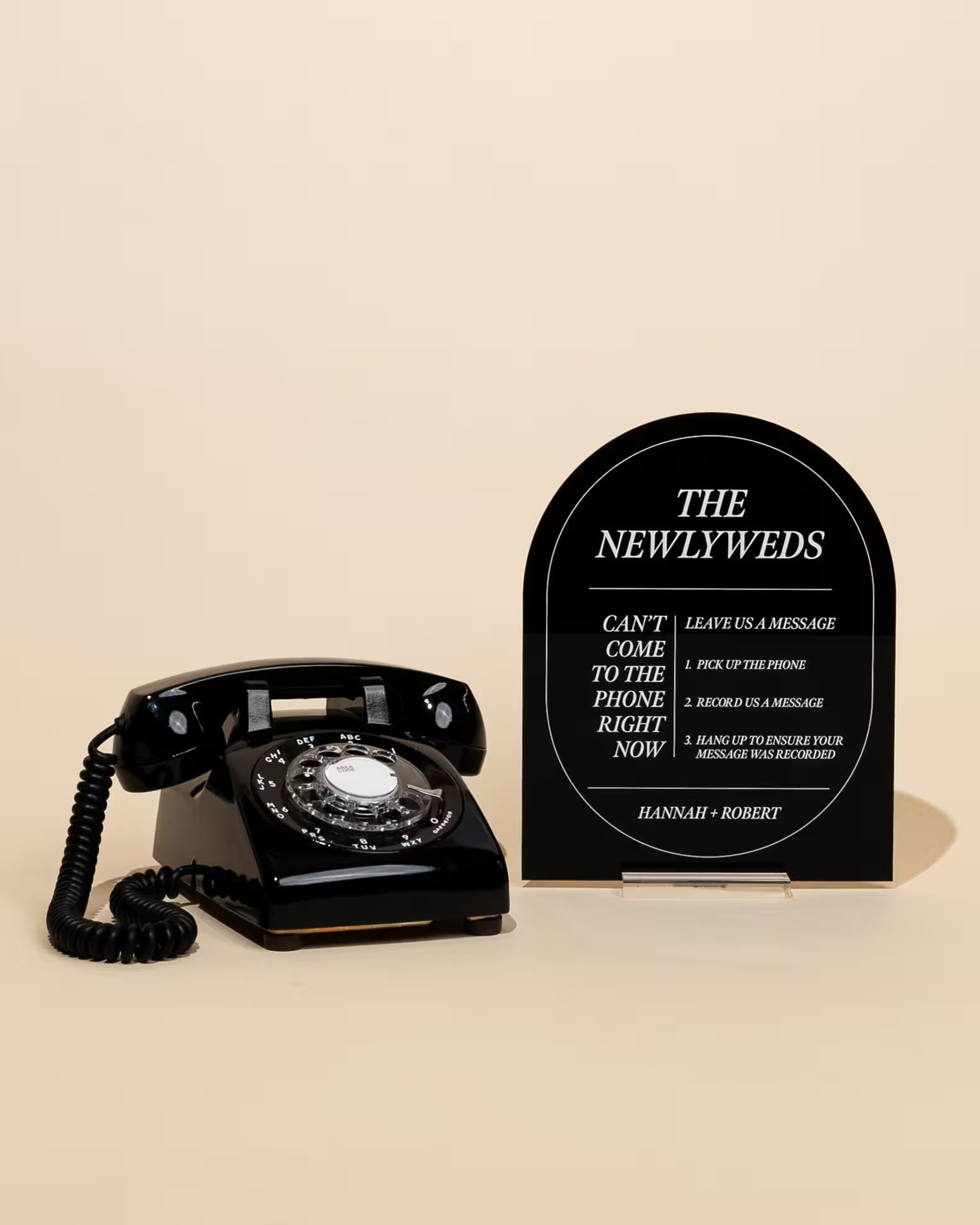 The Icon black arched audio guestbook sign reading The Newlyweds, beside a vintage rotary phone on a beige background