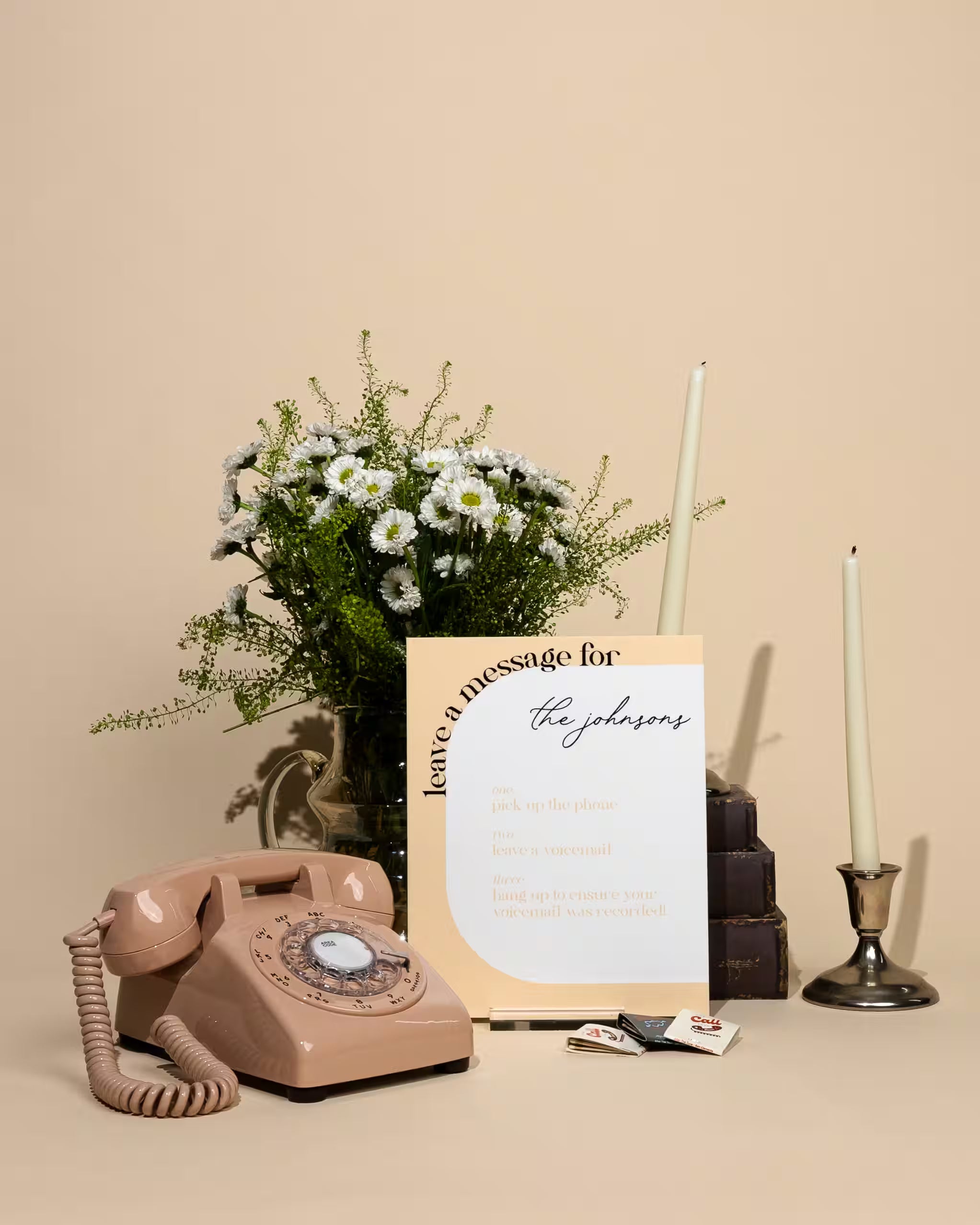 Vintage pink phone, bouquet of flowers, and 'Leave a message for the johnsons' sign on a beige background