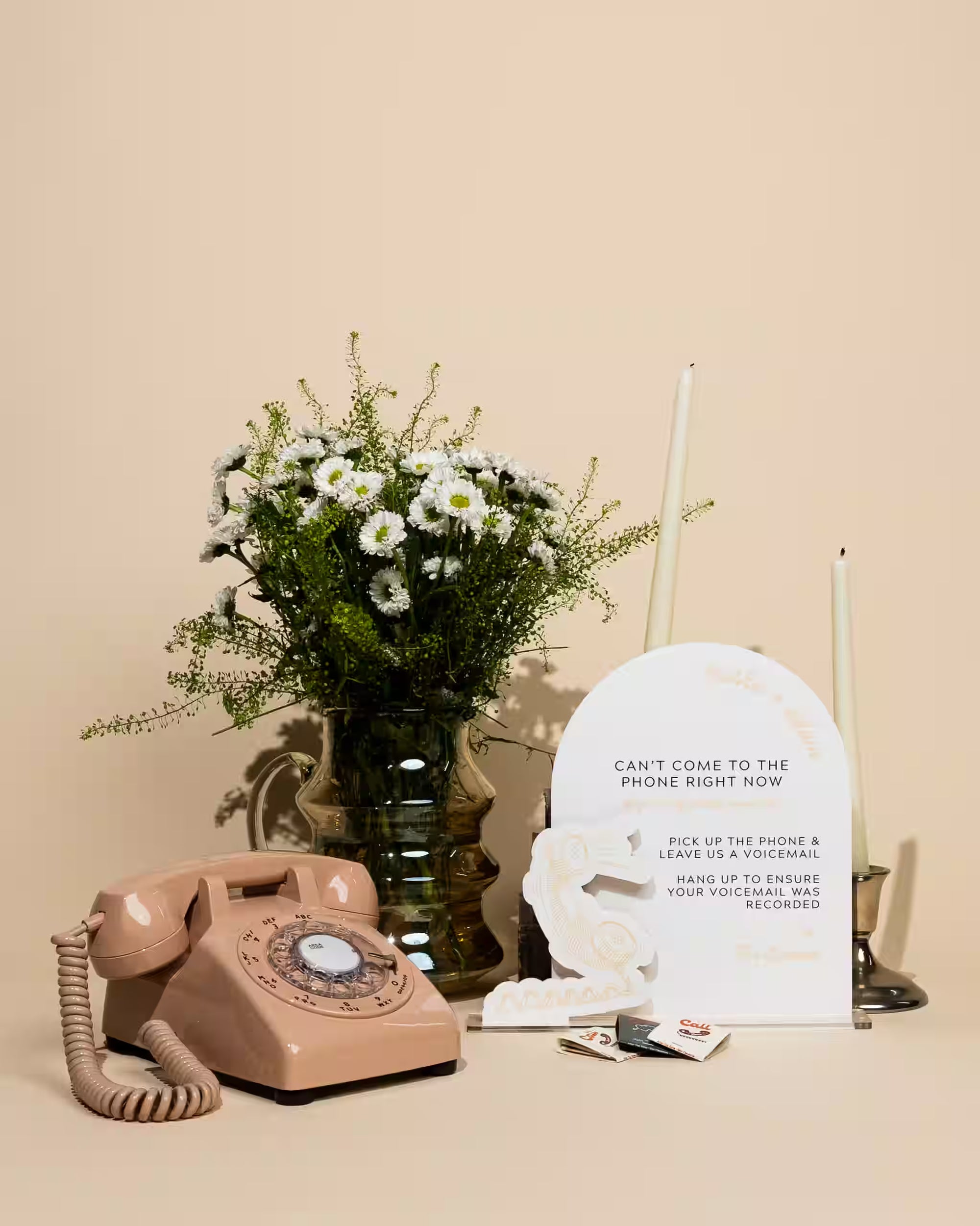 Vintage pink phone, vase with flowers, and 'I'm Out of the Office' sign on a beige surface.