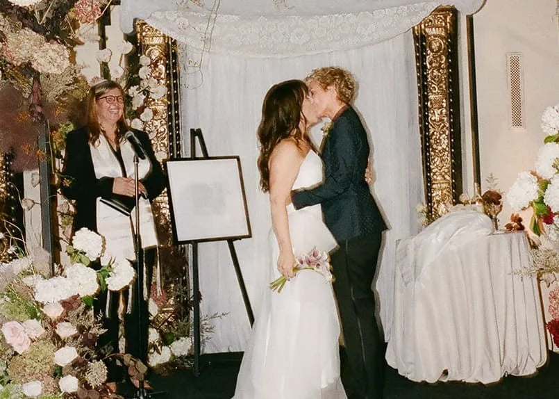 two brides kissing during their wedding ceremony