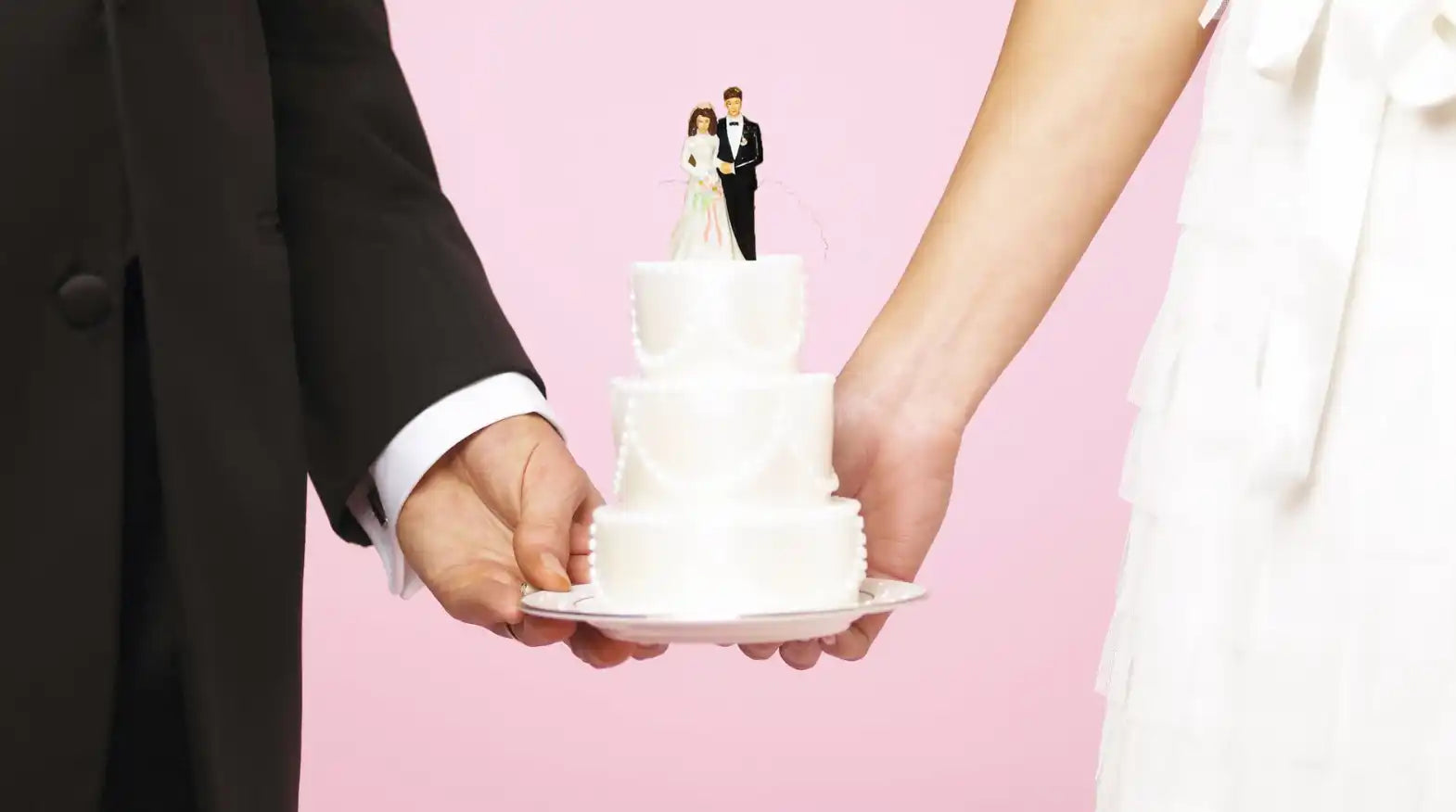 Two people holding a wedding cake with a pink background