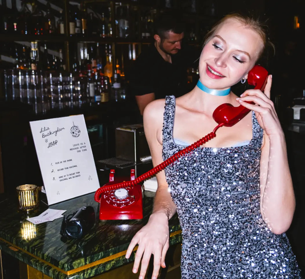 Woman in a sparkly dress holding a red rotary phone in a bar setting