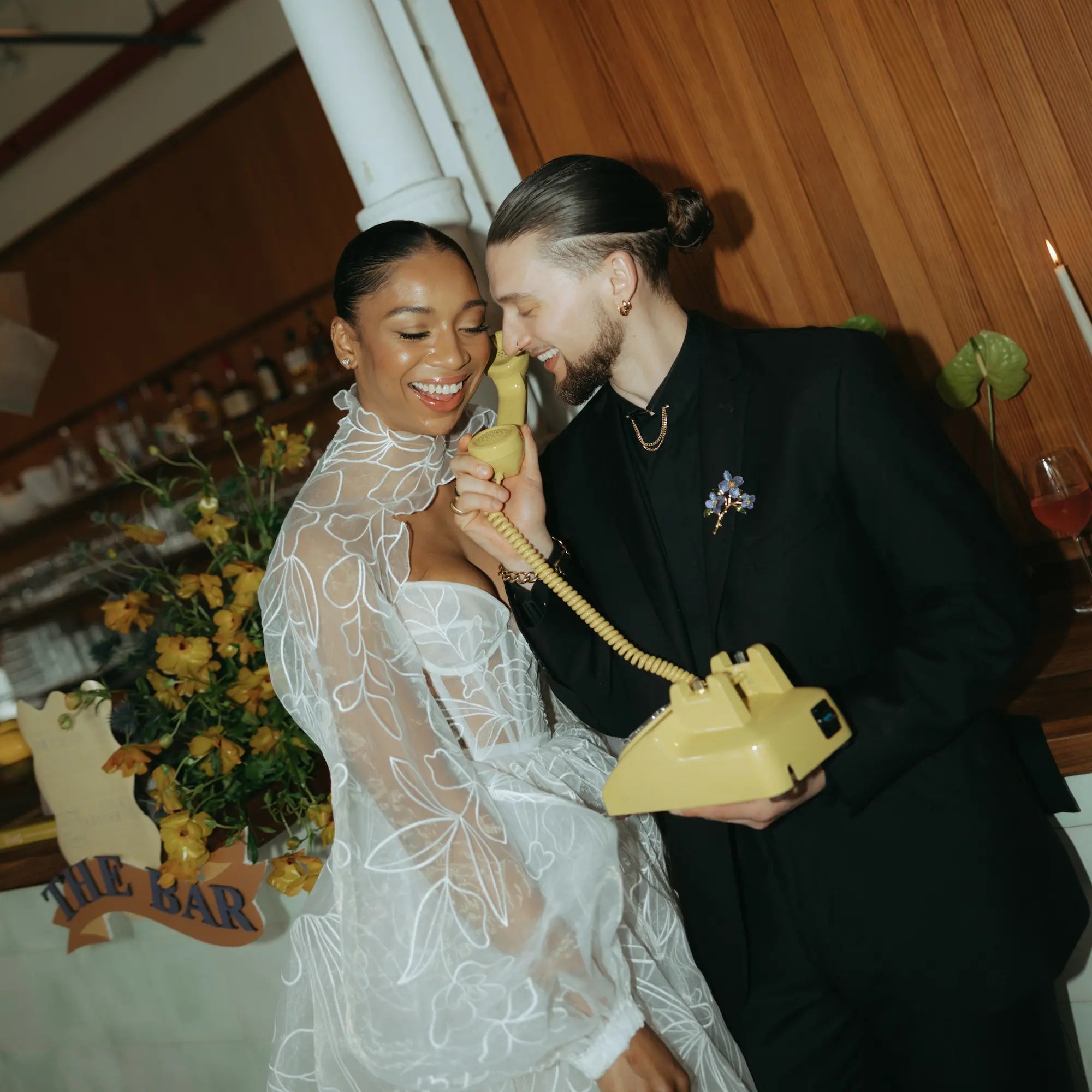 Man and woman holding a yellow rotary phone in a bar setting