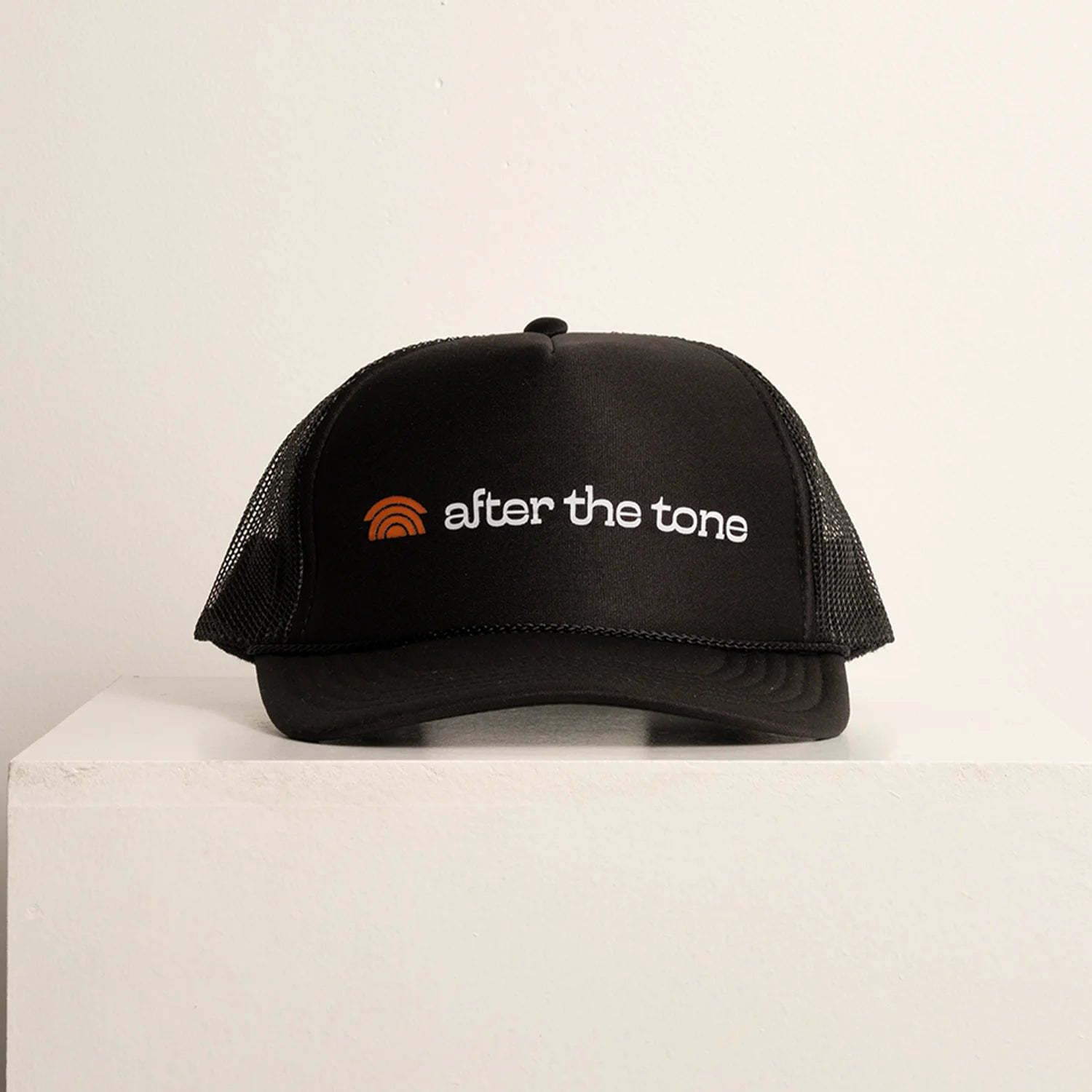 Black cap with 'after the tone' logo on a light beige background