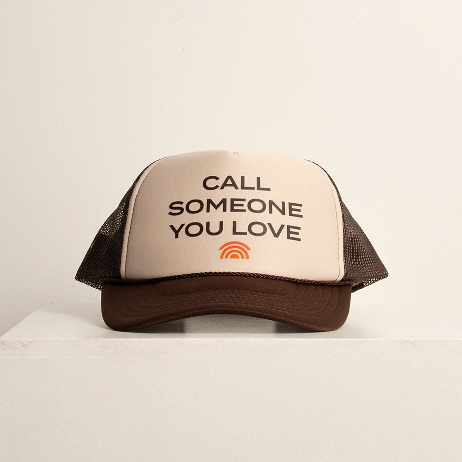 Trucker hat with text 'Call Someone You Love' on a beige background