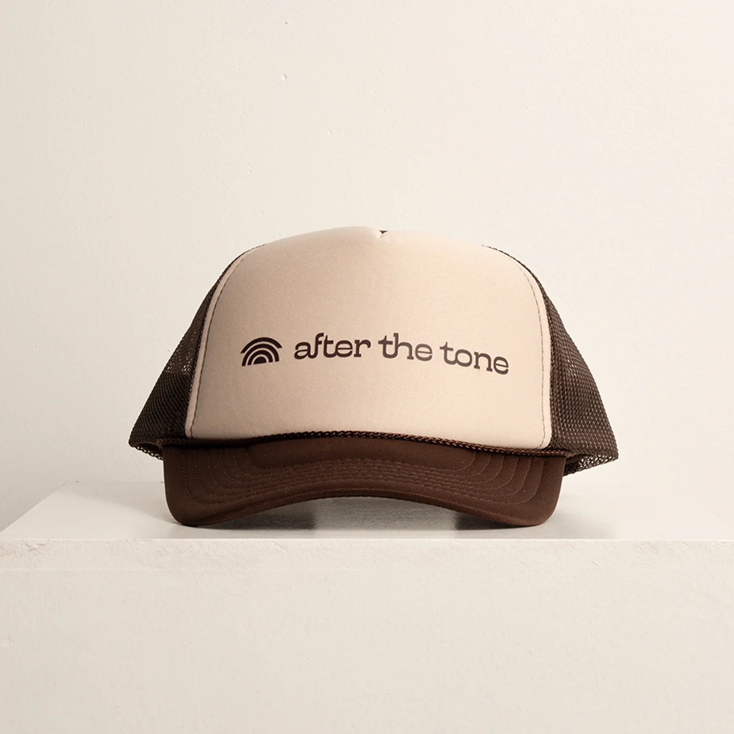 Beige and brown cap with 'after the tone' logo on a beige background