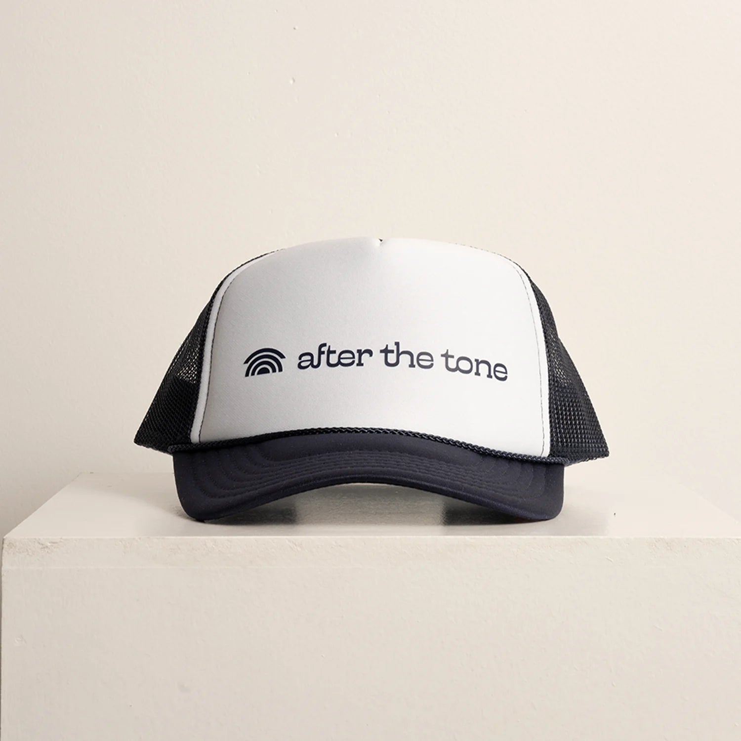 Trucker hat with 'after the tone' logo on a light beige background