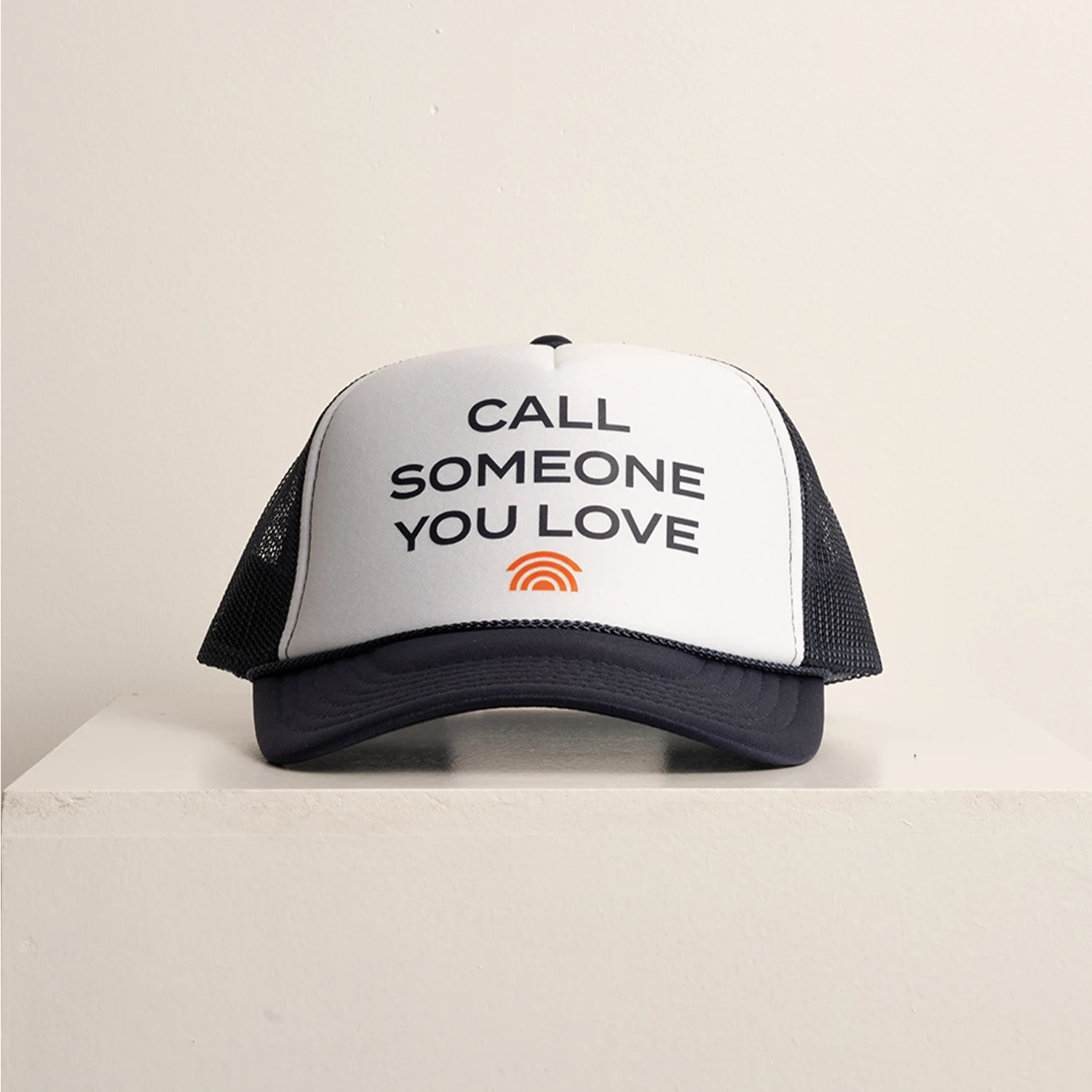 Trucker hat with 'Call Someone You Love' text on a beige background