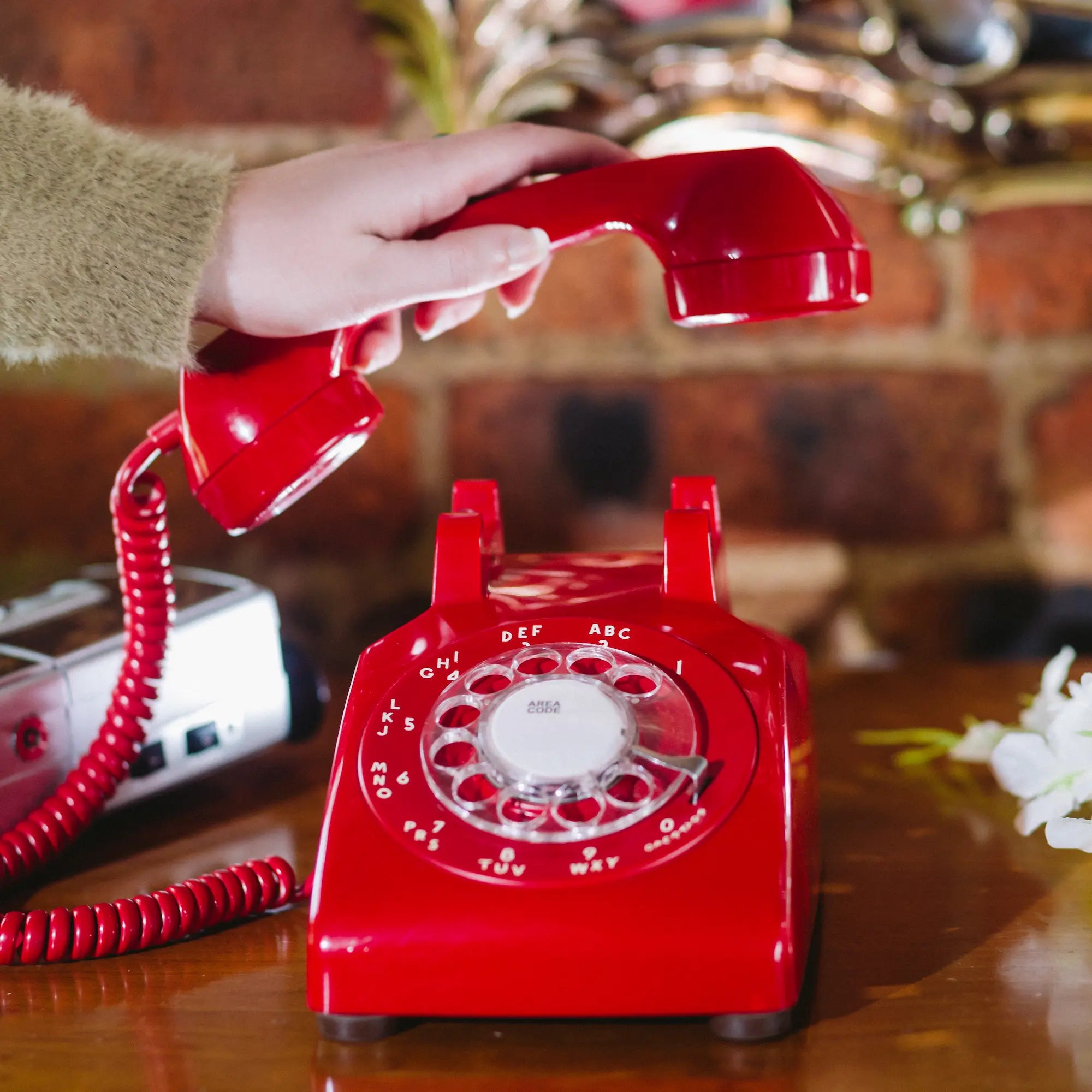 Red rotary phone with a hand lifting the receiver on a wooden surface.