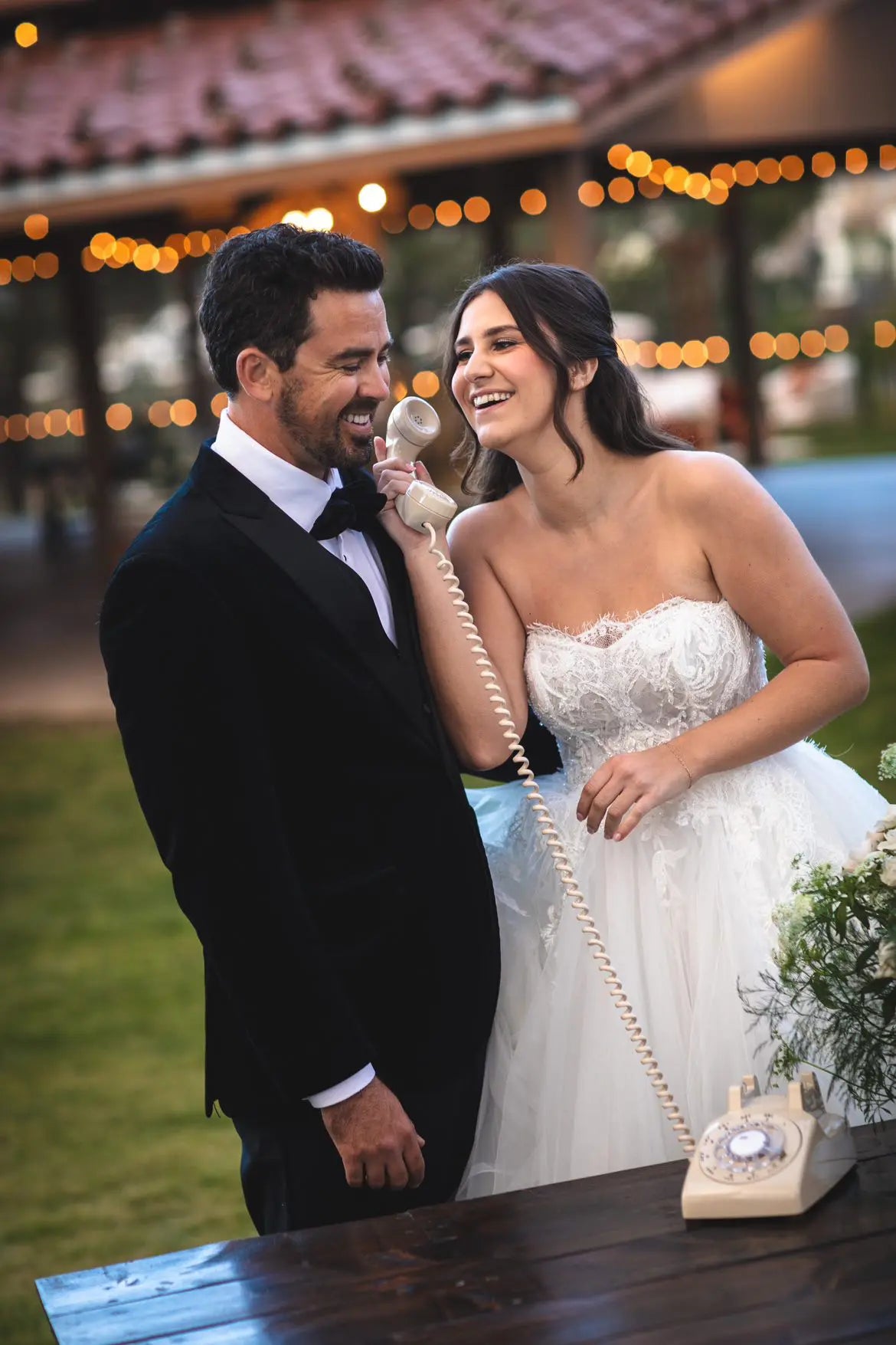 Man and woman in wedding attire with a vintage phone at a wedding reception.