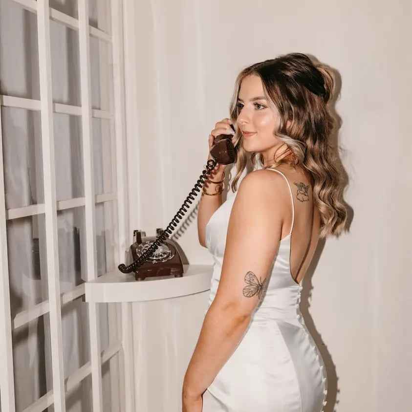 A woman in a white dress using a brown vintage rotary phone audio guestbook.