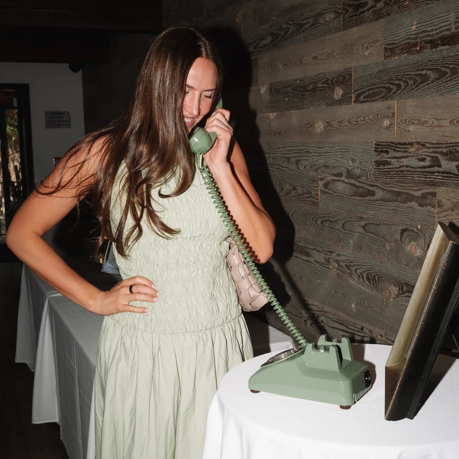 Woman in a green dress using a vintage green phone at a table with a wooden wall background