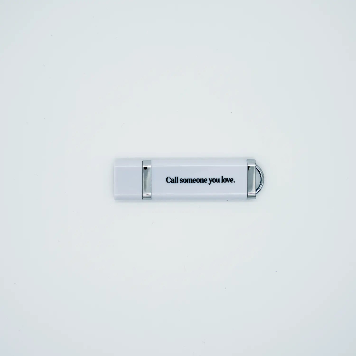 White USB drive with text 'Call someone you love' on a light gray background