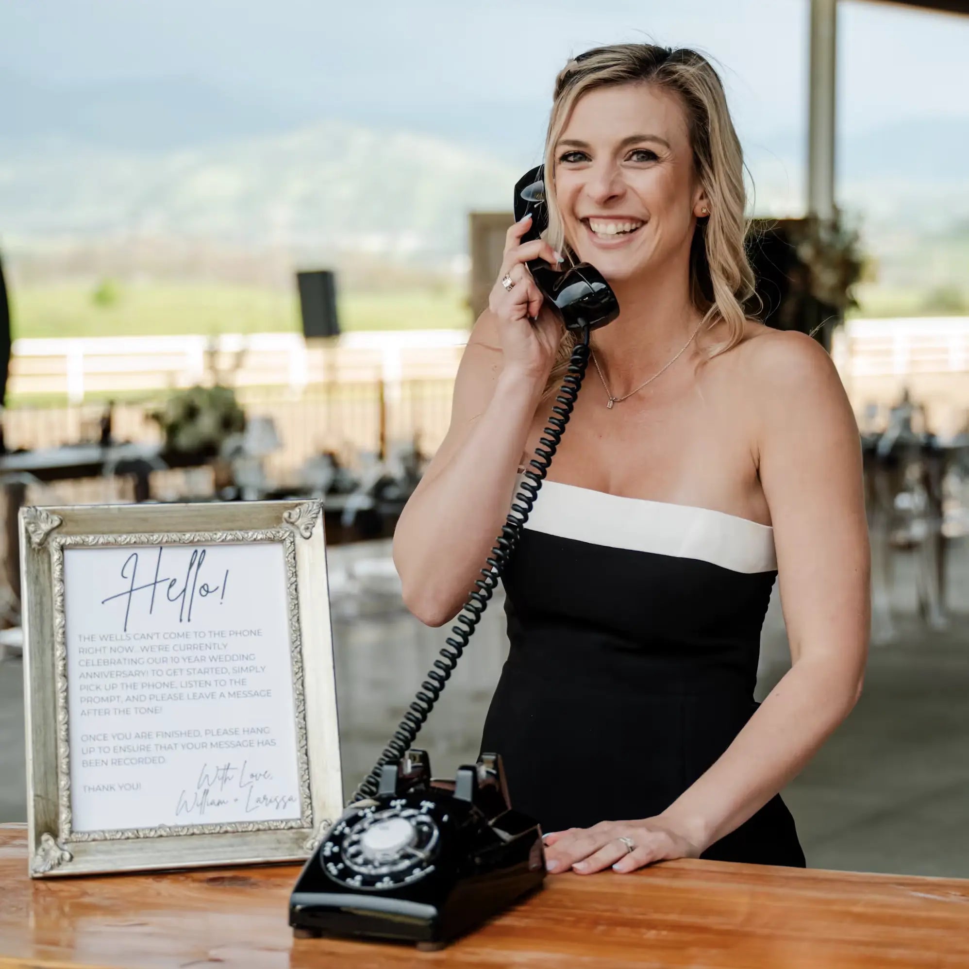 Woman in a black and white dress using a vintage black telephone at an outdoor event.