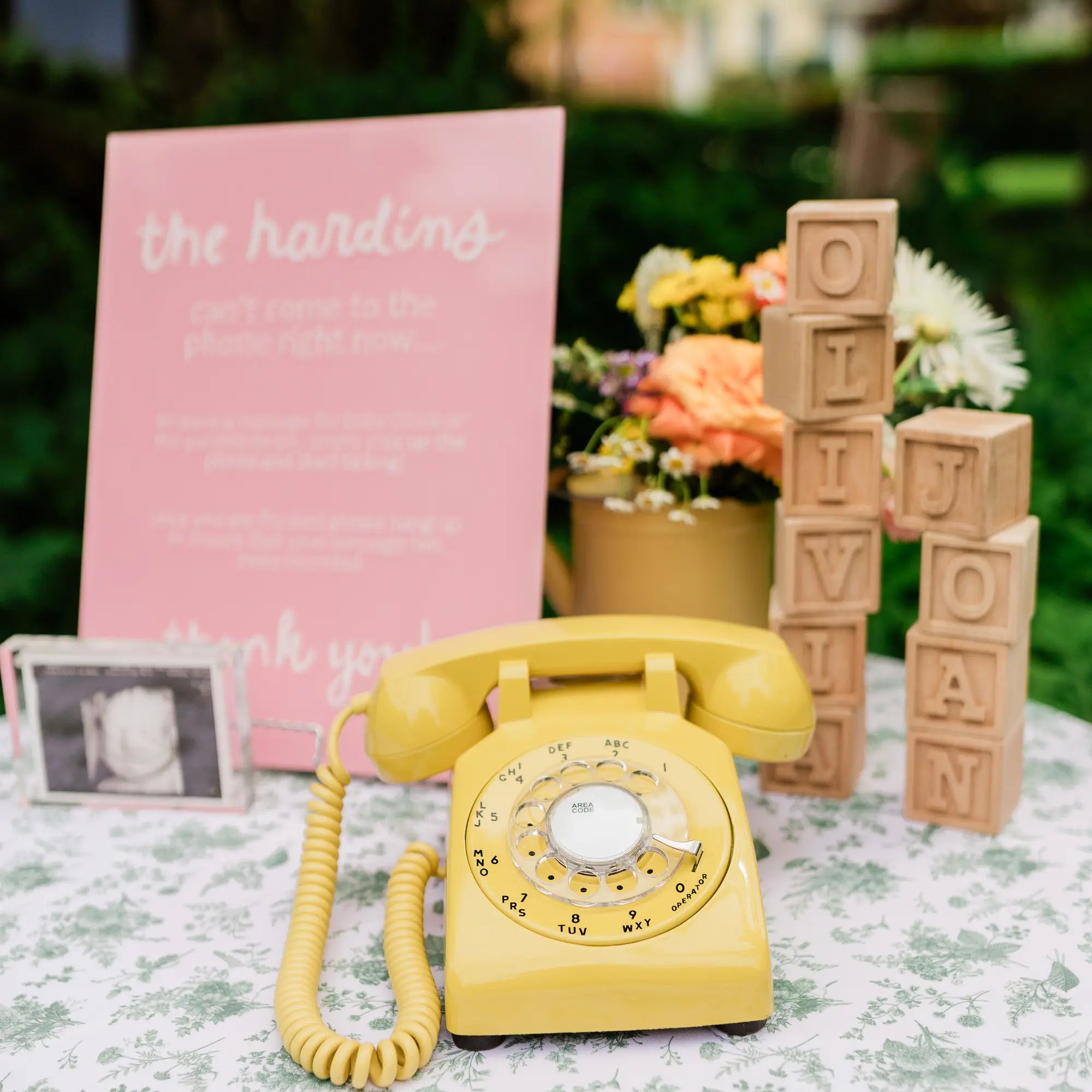 Yellow rotary phone on a table with decorative elements including a pink sign and wooden blocks.