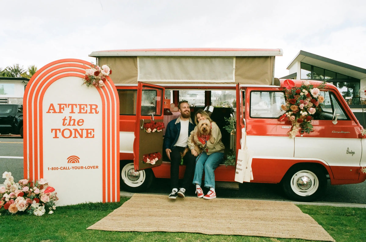 Two people sitting in a red and white van with floral decorations, next to an 'AFTER the TONE' sign.
