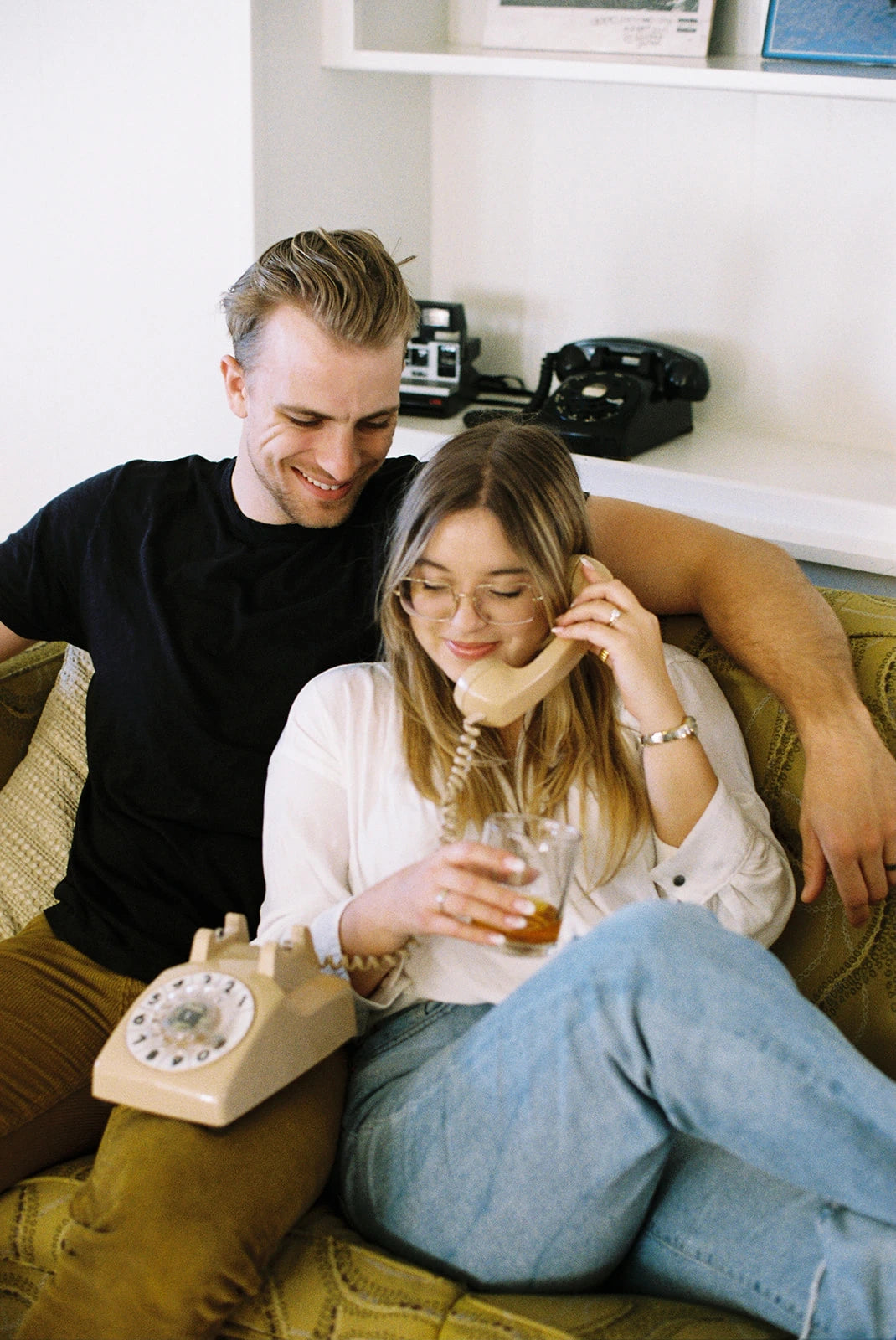 a man and woman sitting on a couch holding a beige rotary phone