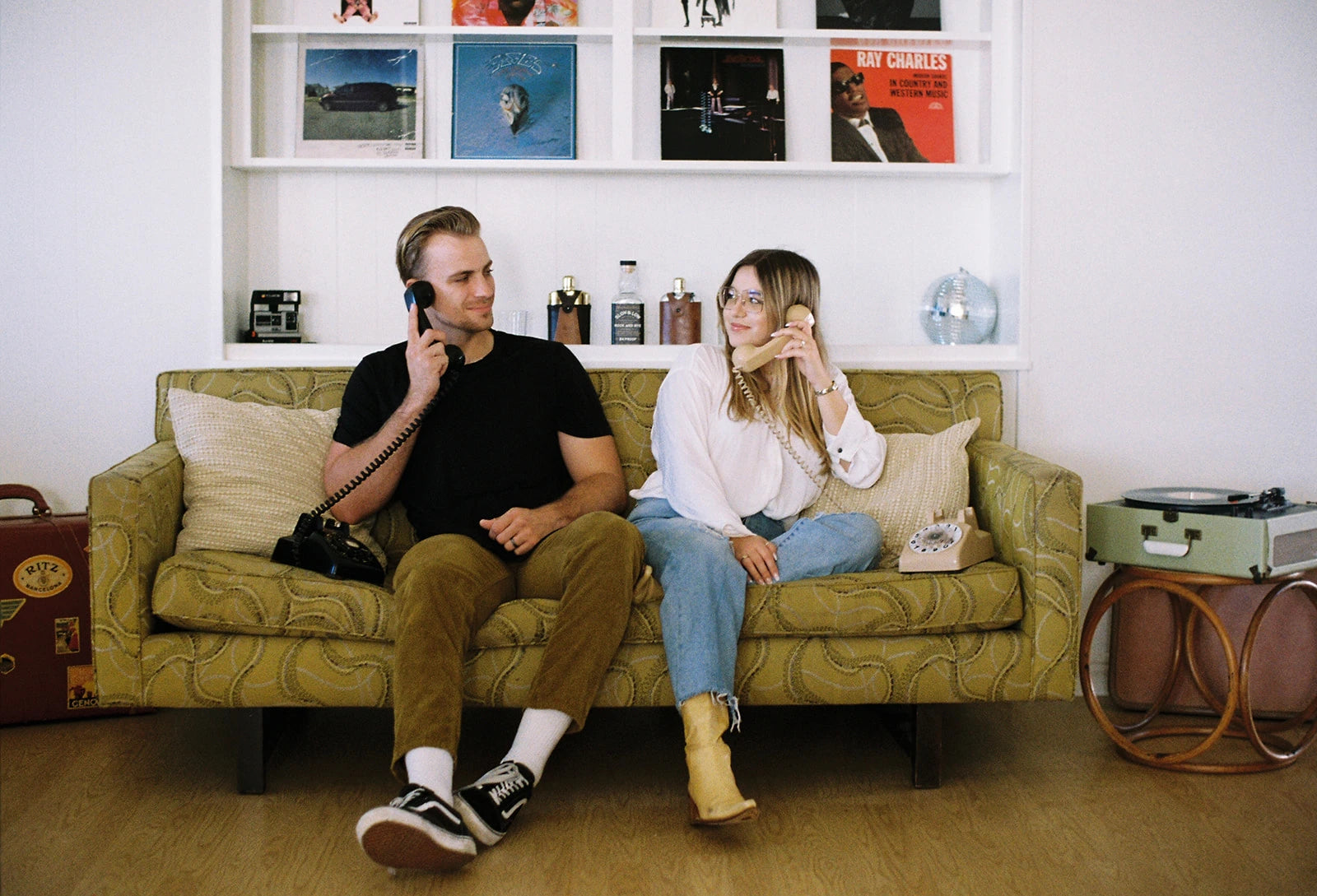 a man and woman sitting on a green couch holding rotary phones