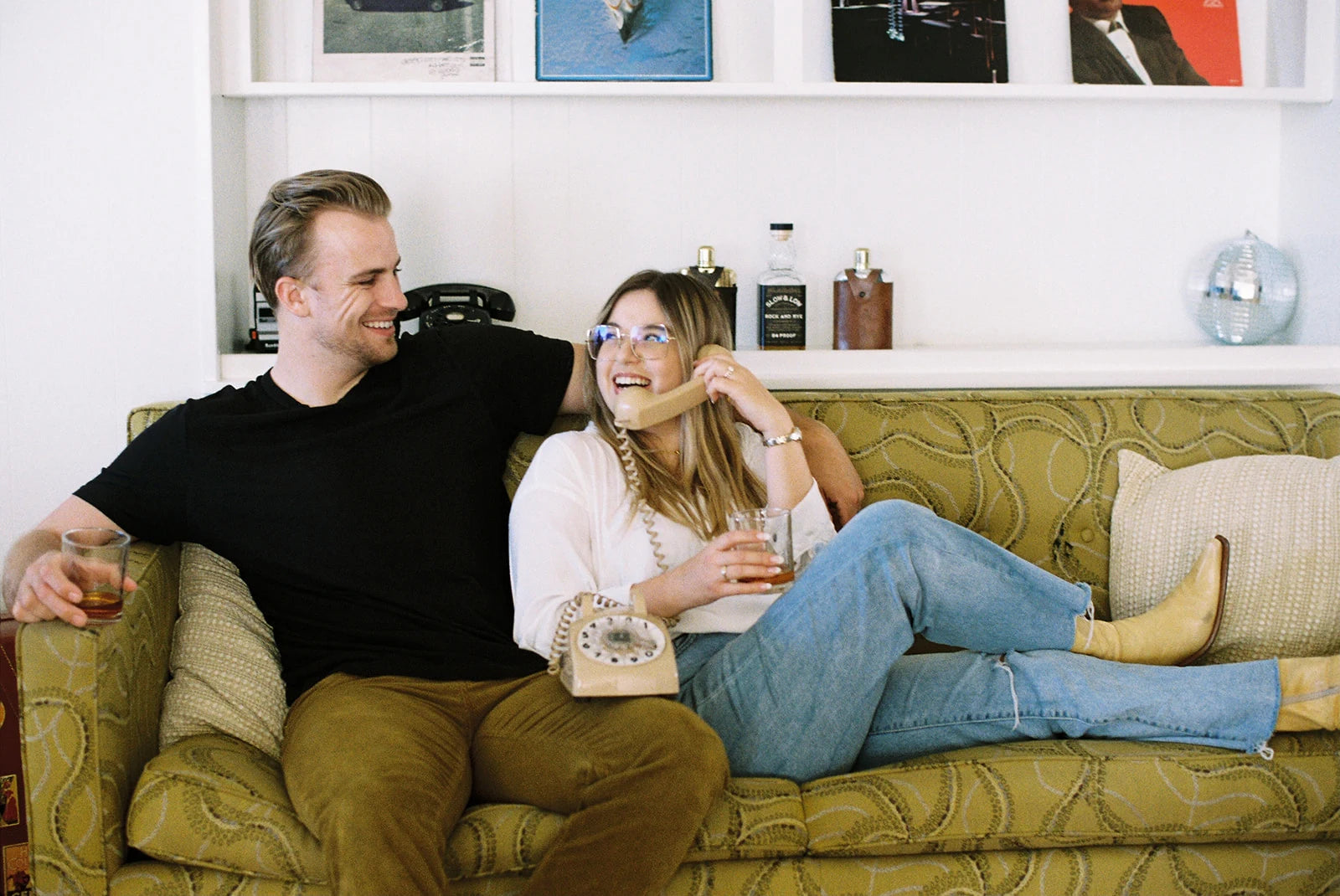 Two people sitting on a couch in a living room with a shelf in the background.