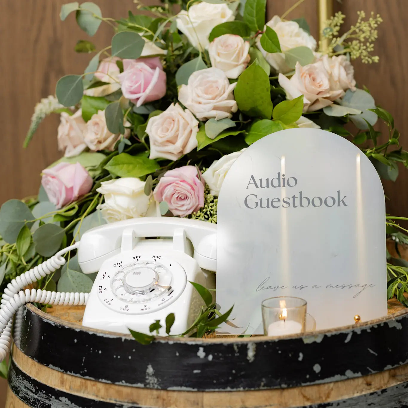 Decorative setup with flowers, vintage phone, and 'Audio Guestbook' on a wooden barrel.