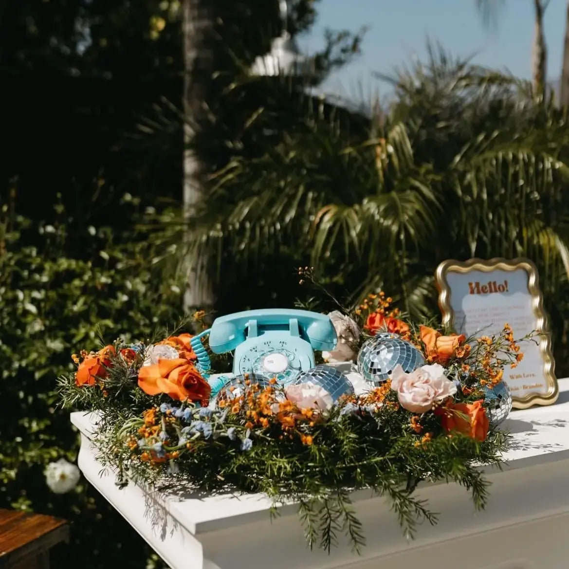 A blue rotary phone on a white table surrounded by flowers and disco balls.