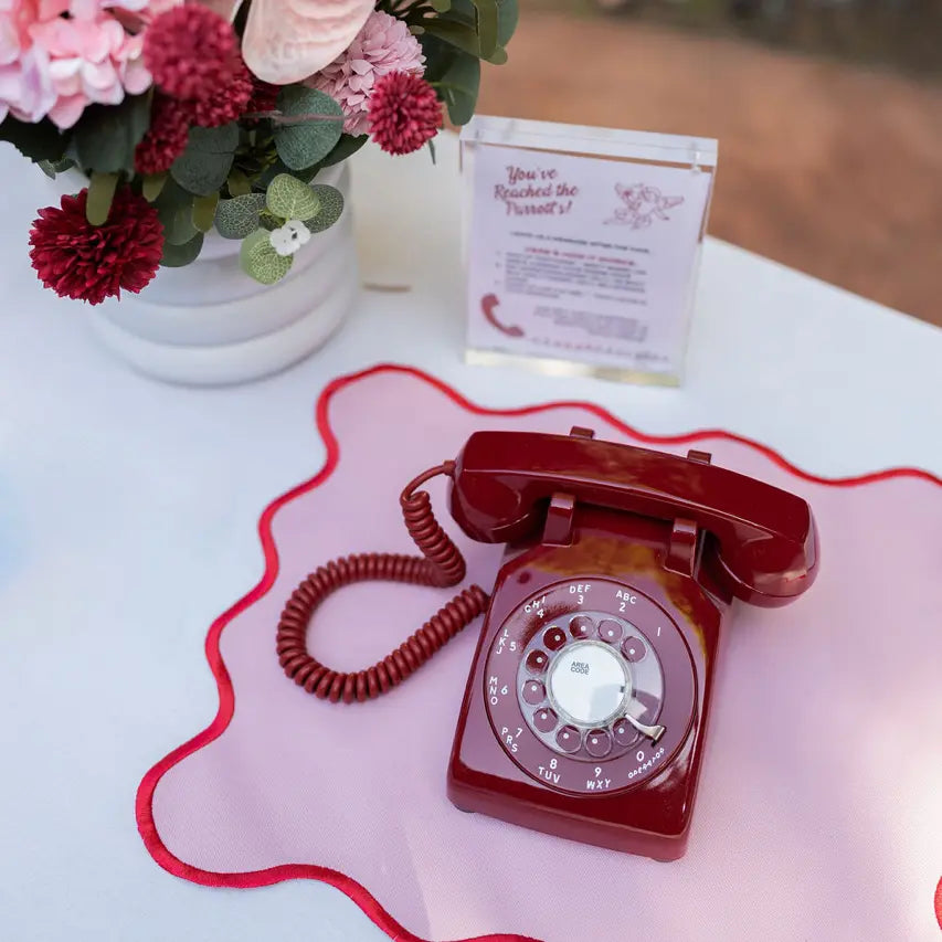 Vintage red rotary phone on a white surface with flowers and a card in the background