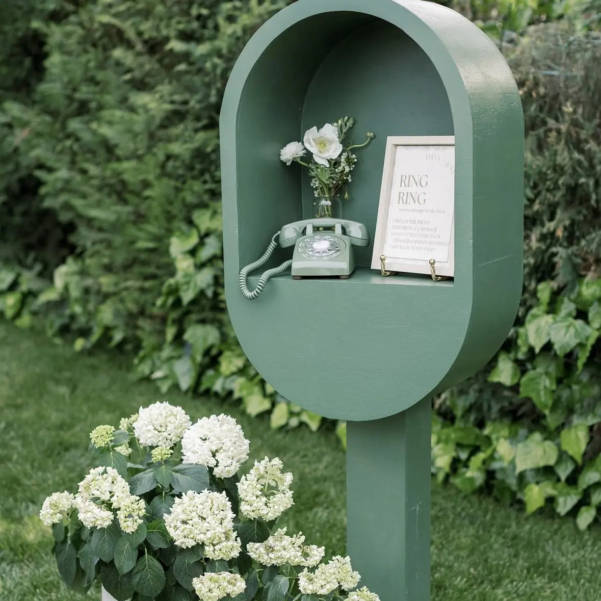 A green rotary phone audio guestbook in a green stand with a sign and flower as decoration.