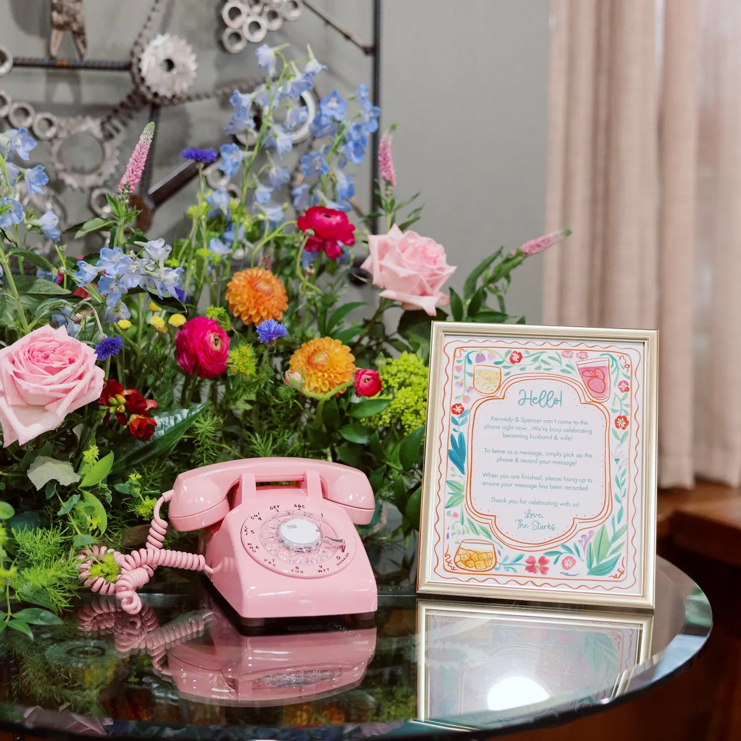 Pink rotary phone on a glass table with flowers and a sign.
