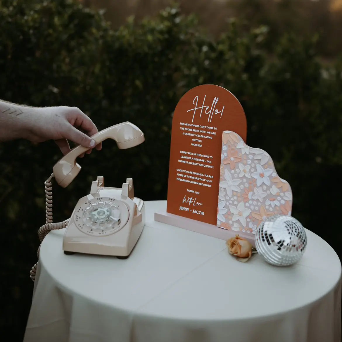 A cream rotary phone on a table with a sign and a disco ball as decoration.