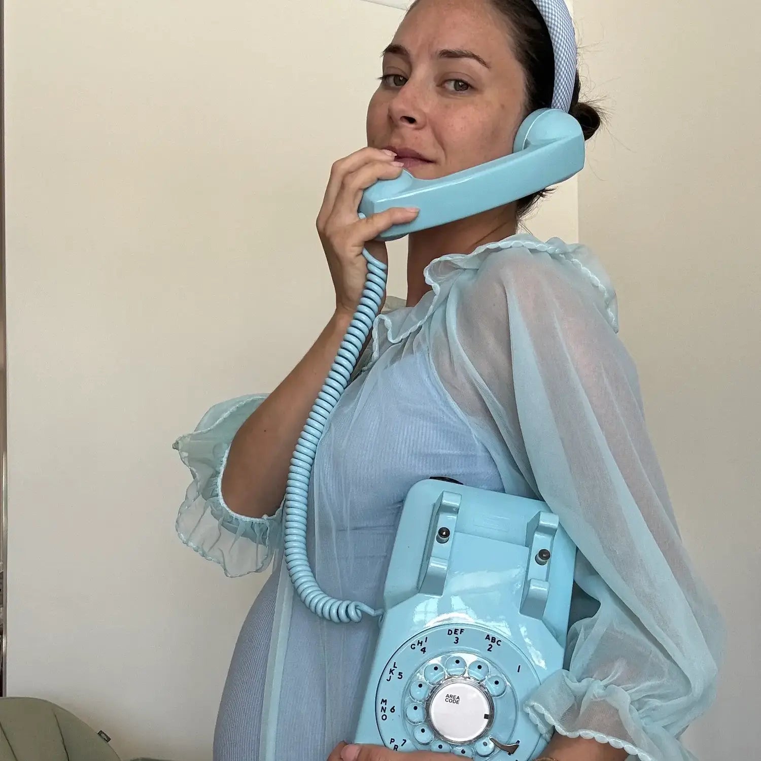 Woman in a light blue dress holding a matching vintage-style telephone against a plain background