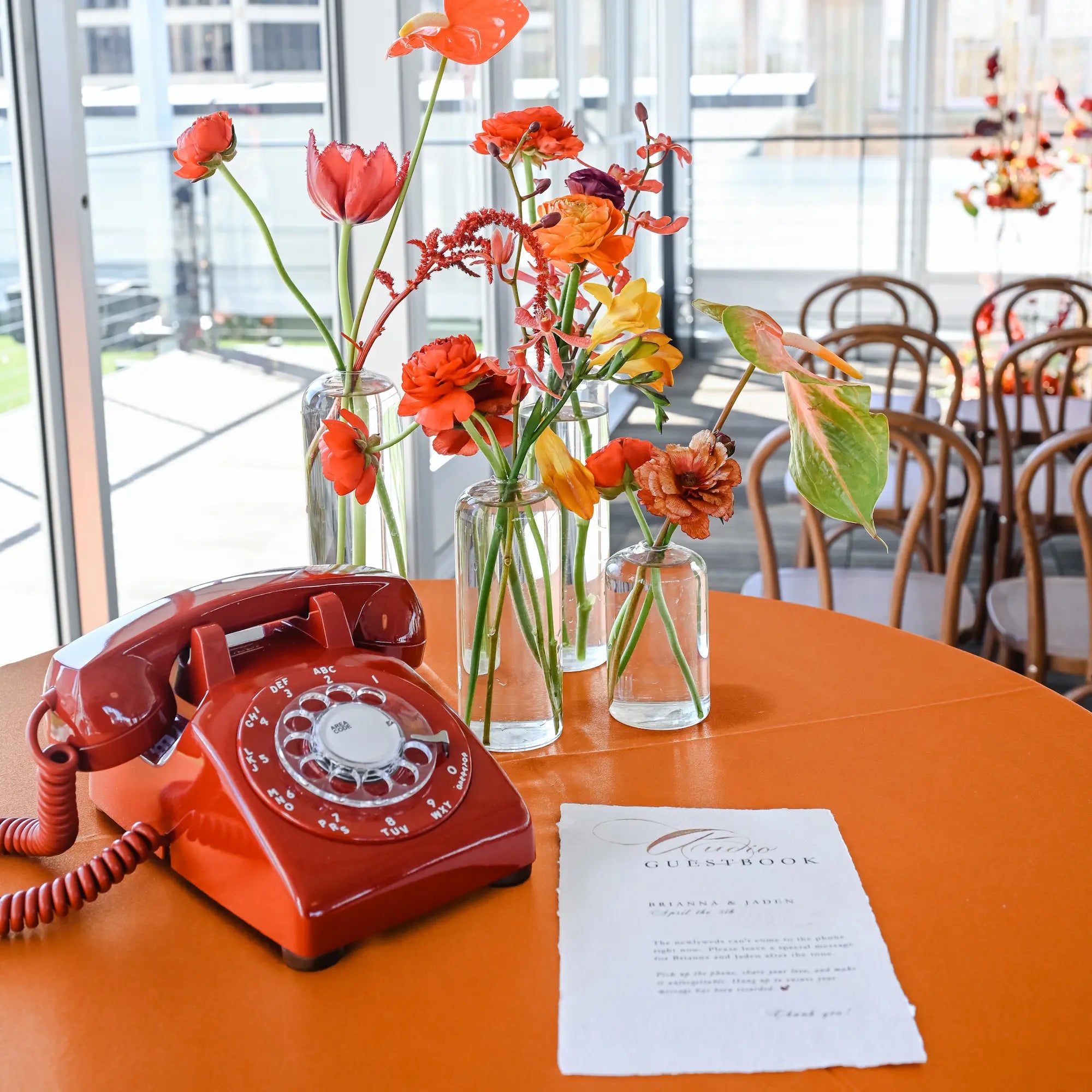 Vintage red rotary phone on an orange table with flowers and a menu in a restaurant setting.