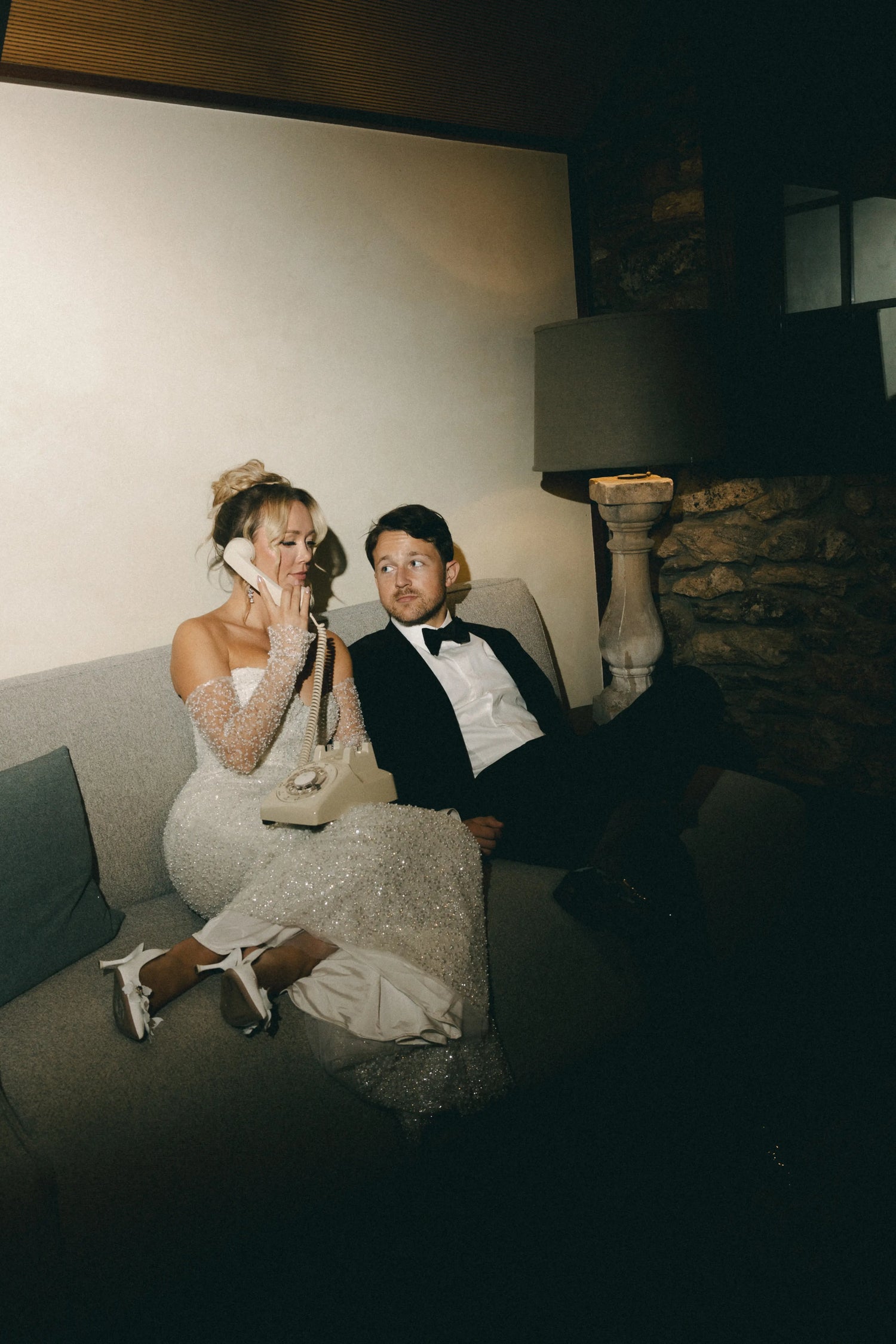 Couple sitting on a couch in a dimly lit room with a stone wall background using an audio guestbook