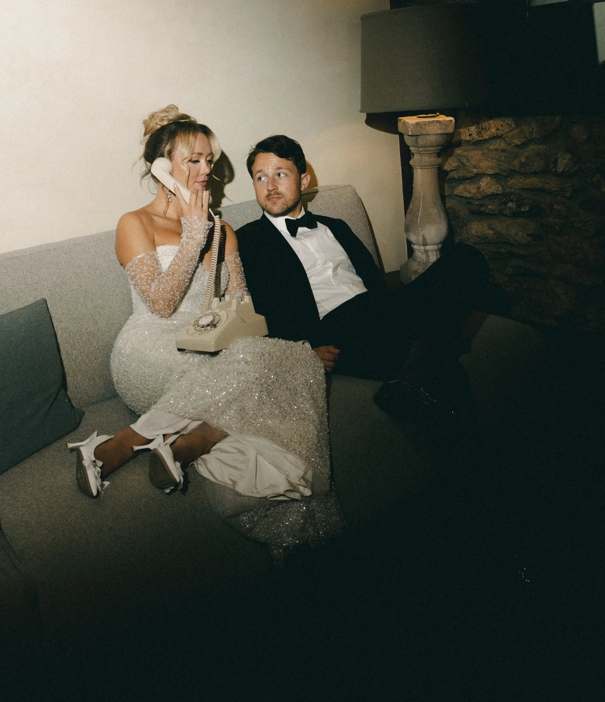 Couple sitting on a couch in a dimly lit room with a stone wall background using an audio guestbook
