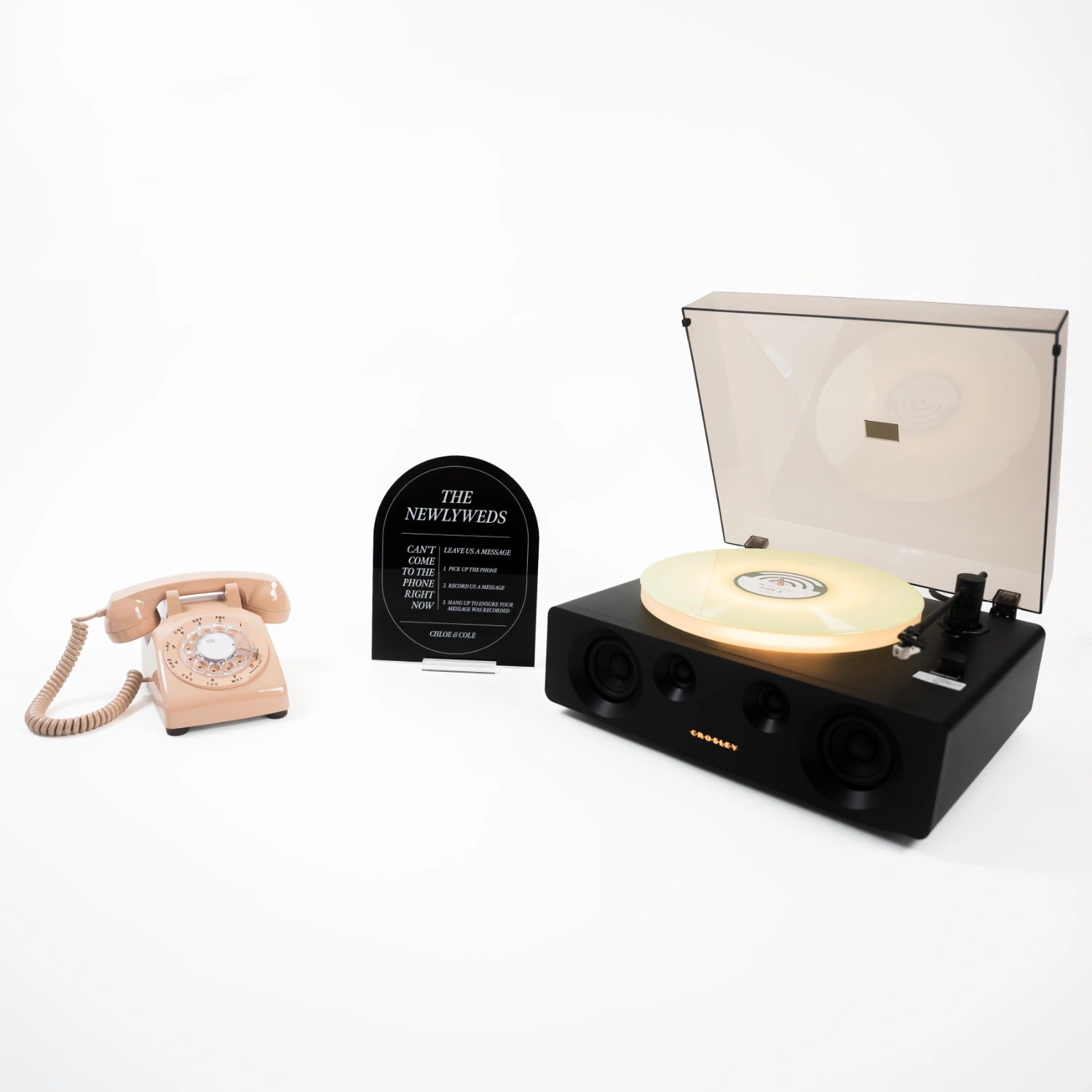 The Rod bundle: a beige rotary phone audio guestbook, a black Icon acrylic sign reading The Newlyweds, and a record player spinning a custom vinyl record.
