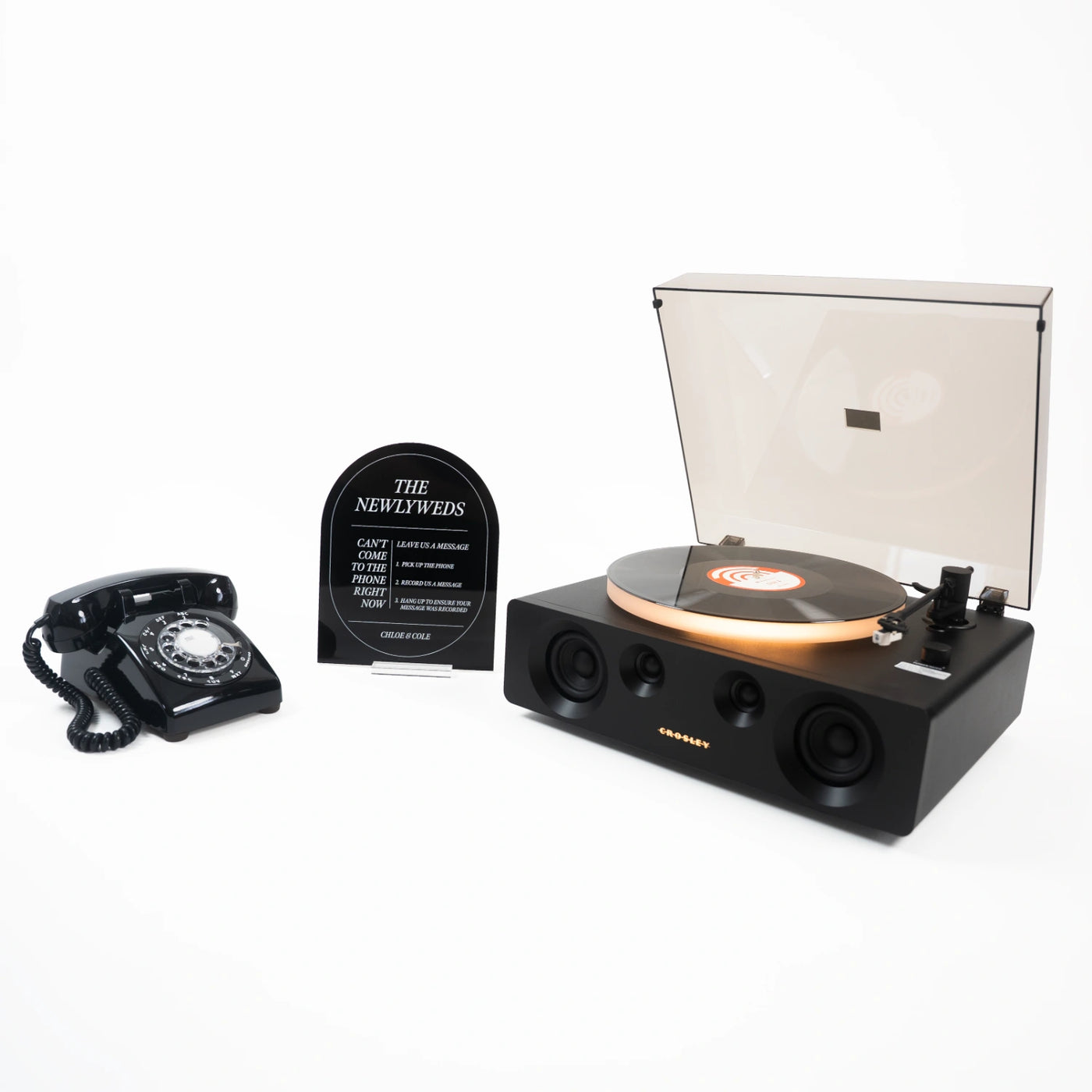 The Dylan bundle: a black rotary phone audio guestbook, a black Icon acrylic sign reading The Newlyweds, and a record player spinning a custom vinyl record.