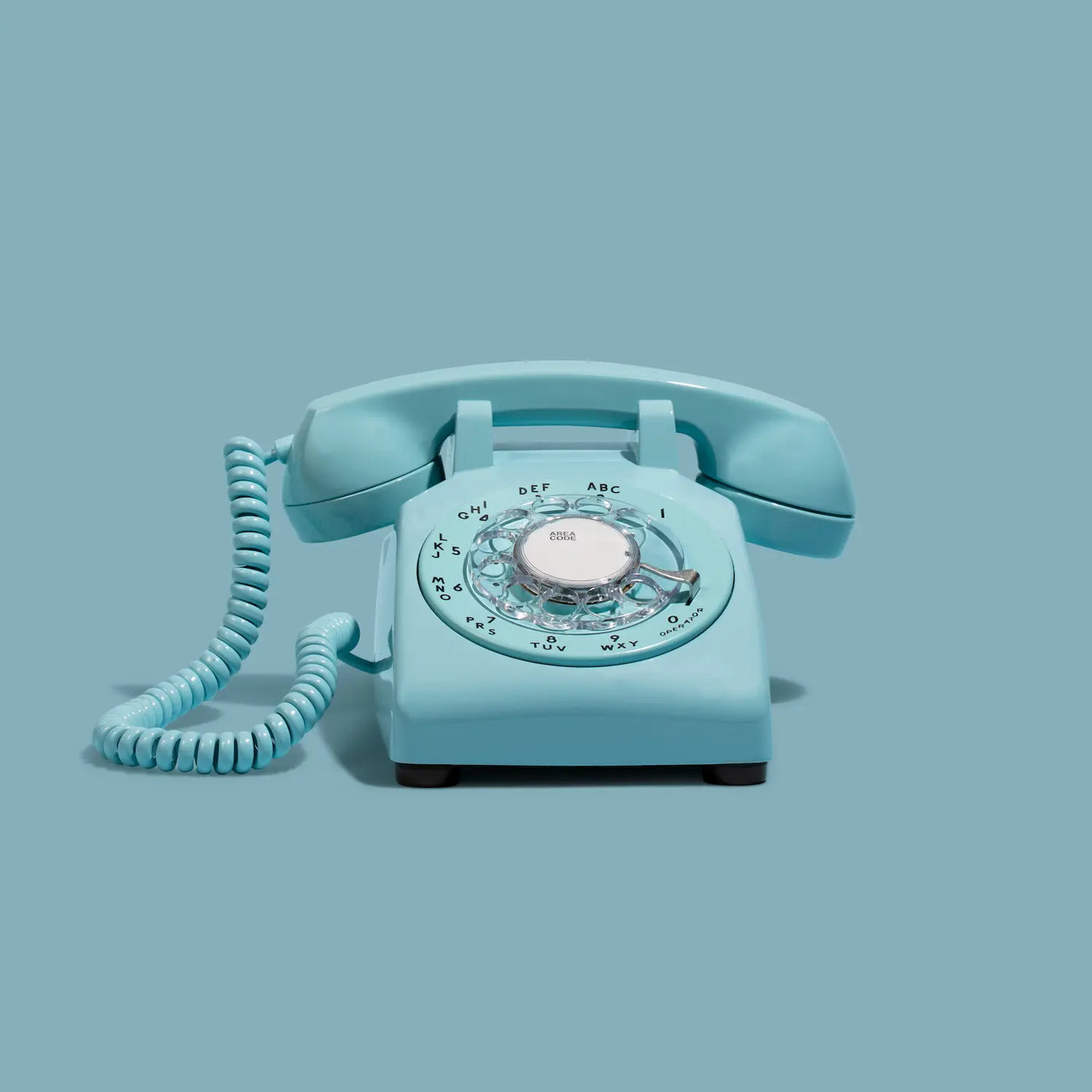 Vintage turquoise rotary phone on a light blue background