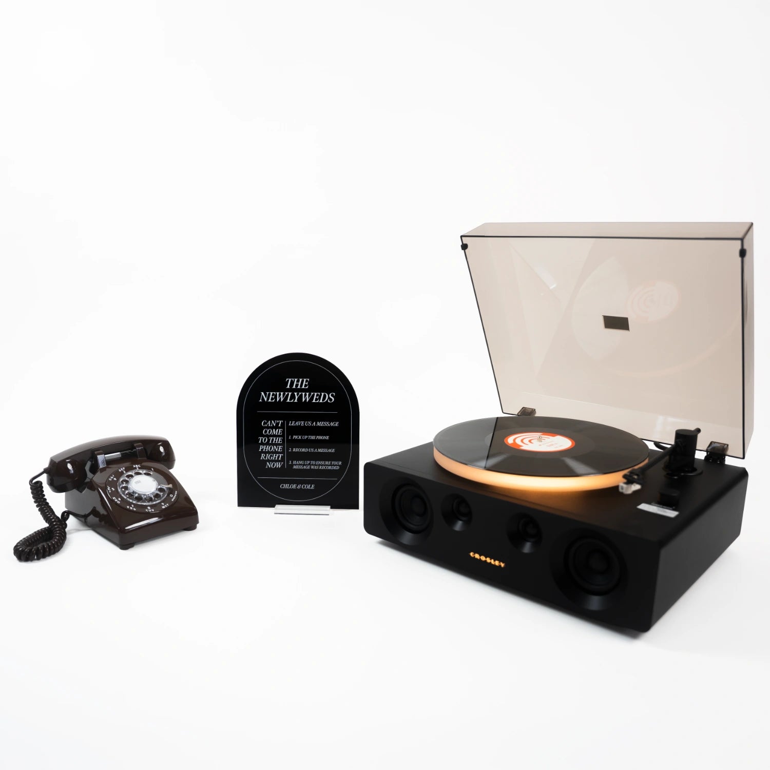 The Neil bundle: a light brown rotary phone audio guestbook, a black Icon acrylic sign reading The Newlyweds, and a record player spinning a custom vinyl record.
