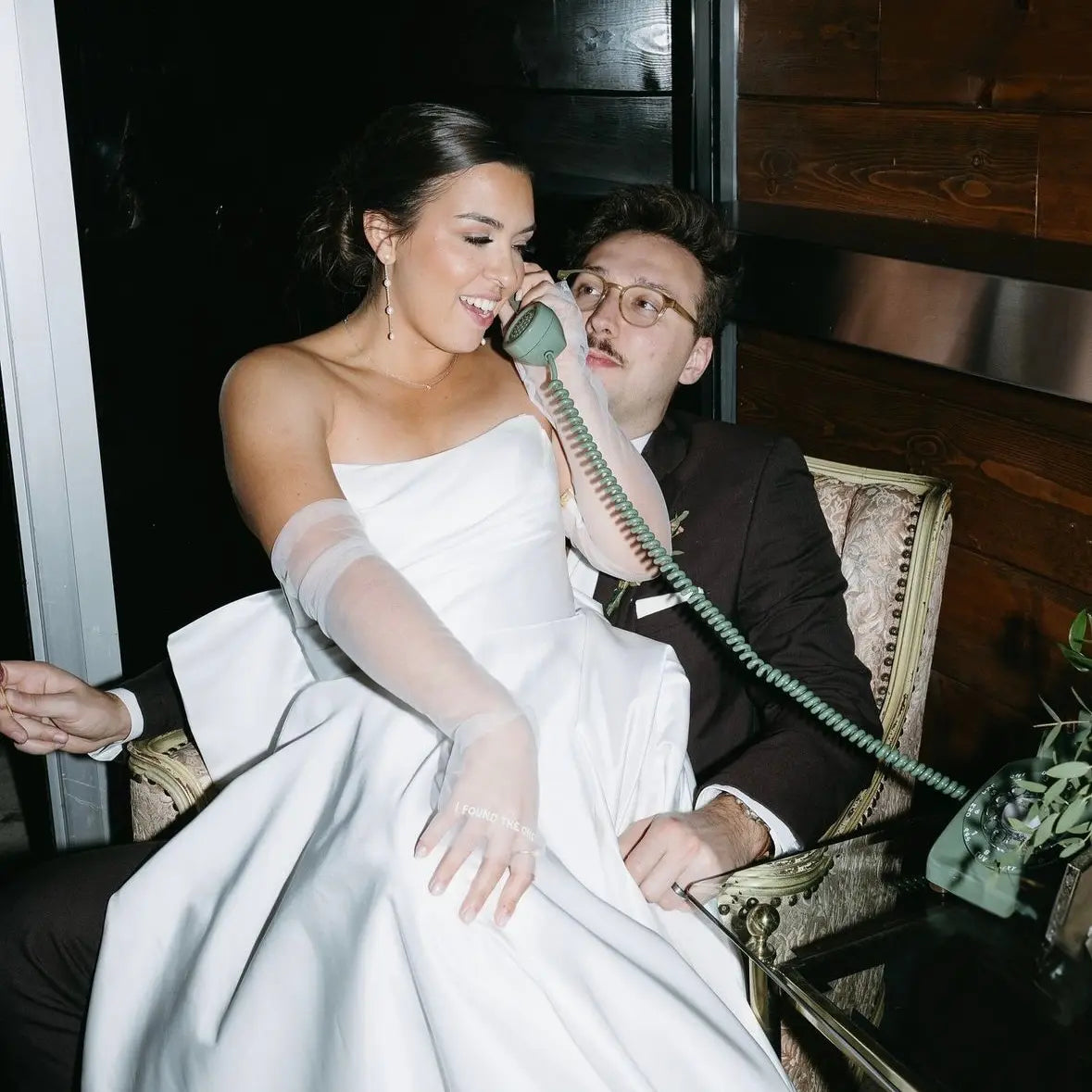 Woman in a white dress and gloves talking on a vintage phone with a man in a suit.